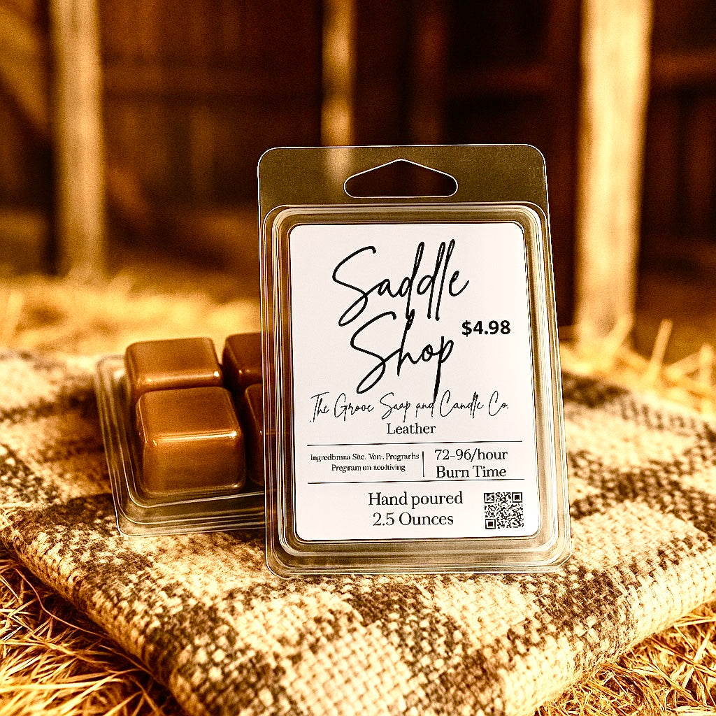 Packaged leather-scented wax melts with 'Saddle Shop' label on a textured surface. Depicts the hand poured 2.5 ounce size of the clamshell