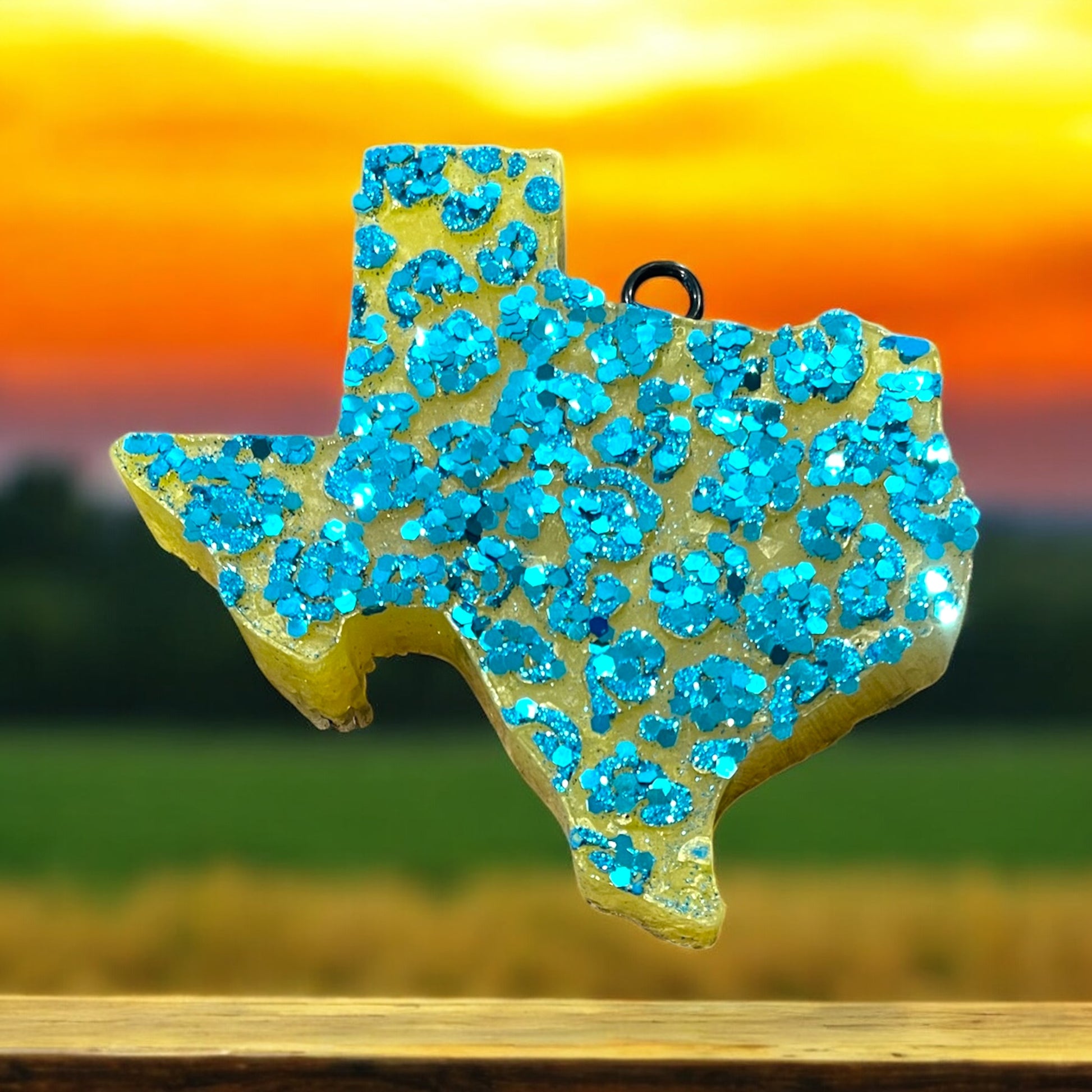 Texas-shaped car freshie with chunky blue glittery pattern on a blurred landscape background