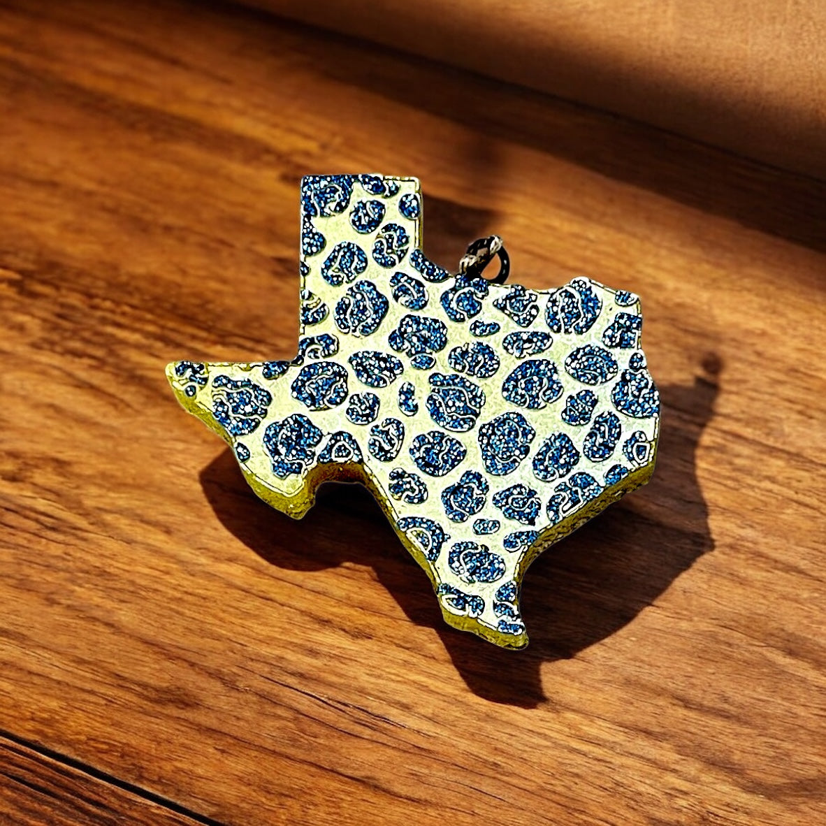 Texas-shaped car freshie in yellow with dark blue glitter on a wooden surface