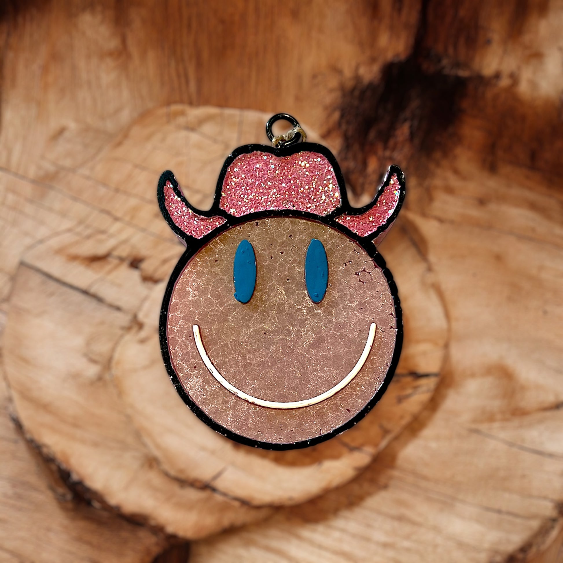 Smiley face car freshie with pink glittery horns on a wooden surface
