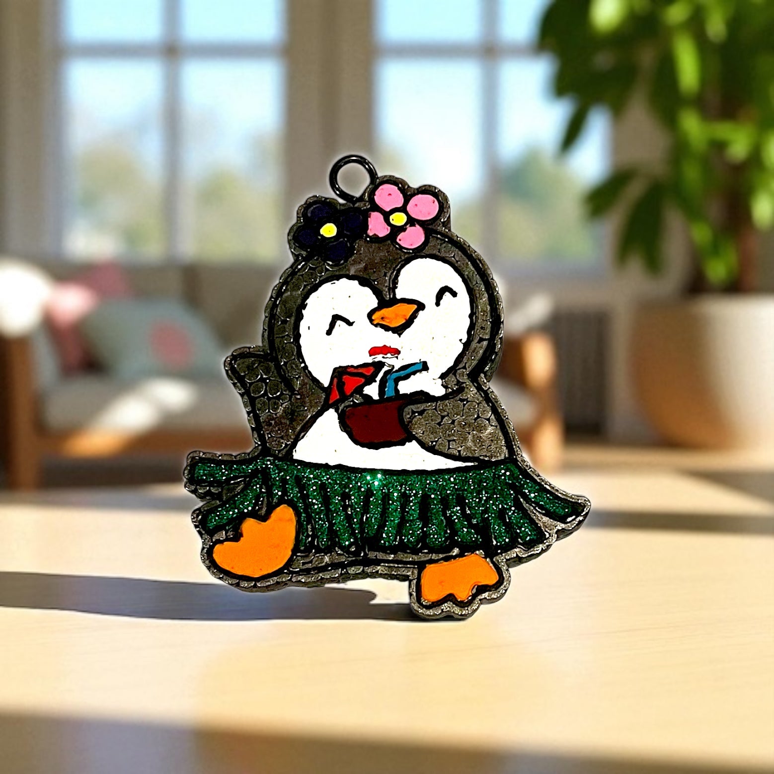Penguin car aroma beads with a green glitter skirt and pink flower on a blurred indoor background