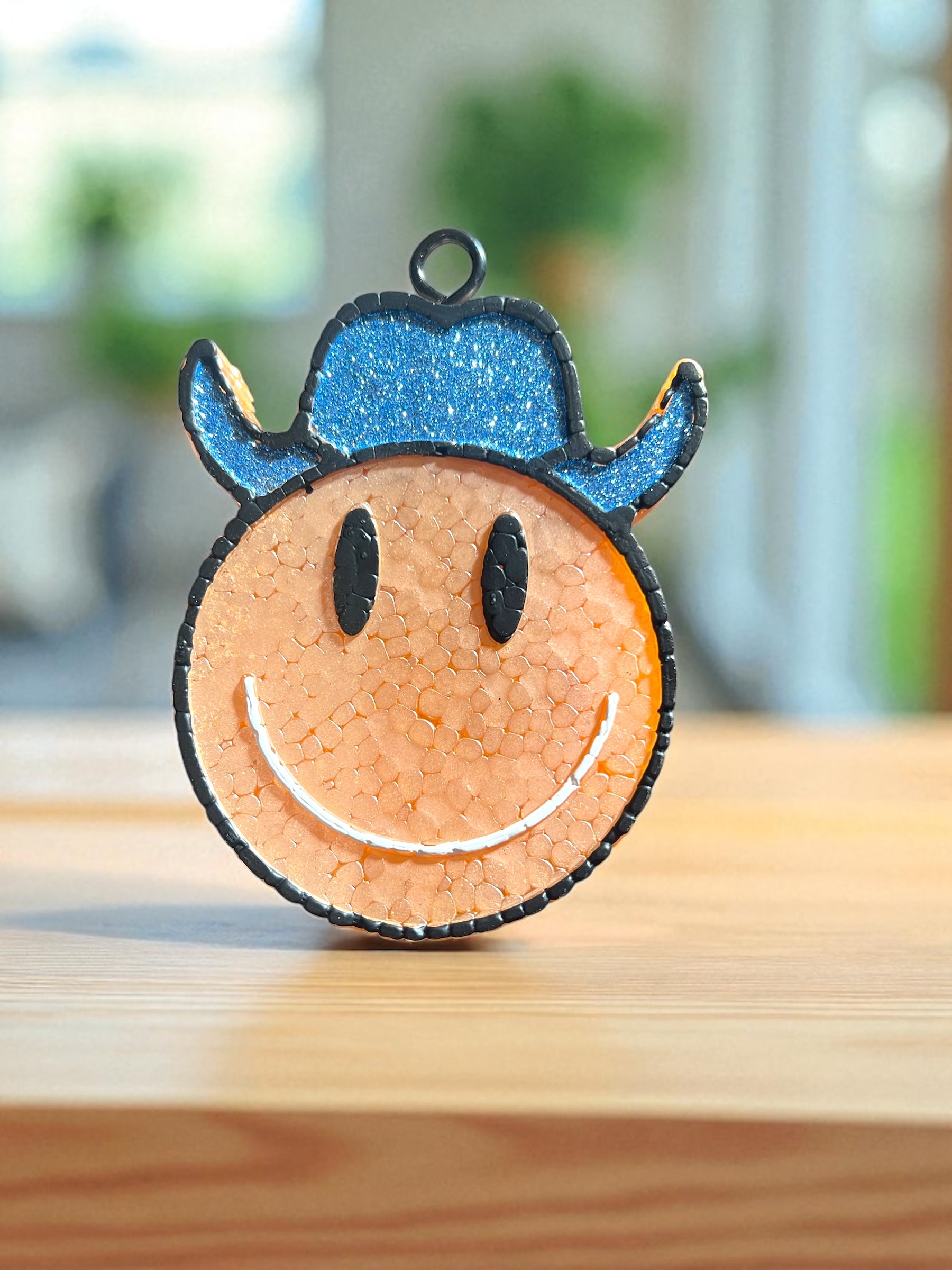 Peach Smiley face western car freshie with blue glitter hat on a wooden surface