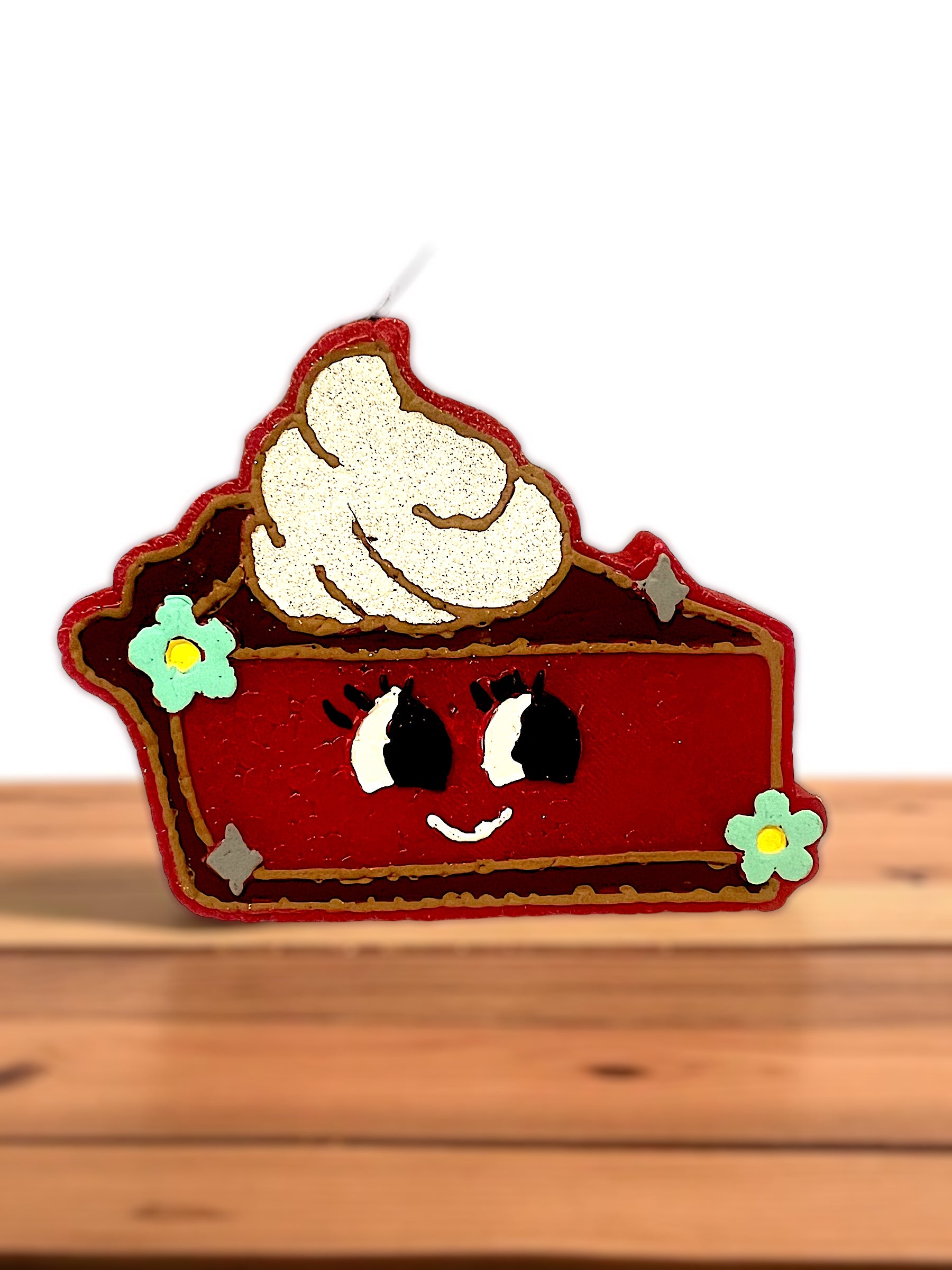 Decorative cherry pie slice with a face on a wooden surface. Showing the details of this car freshie up close.