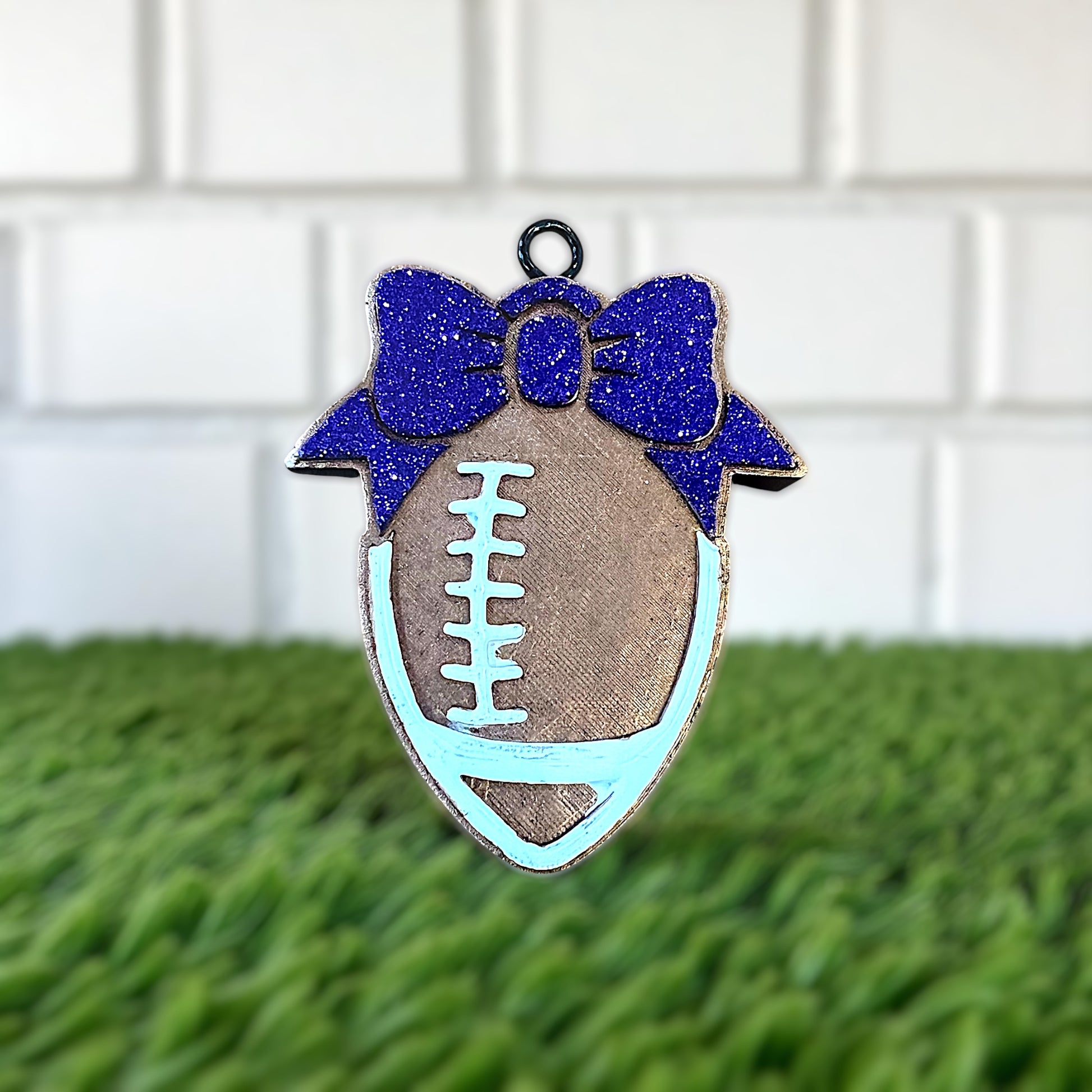 Decorative football car aroma beads with a purple glitter bow on a grassy surface.