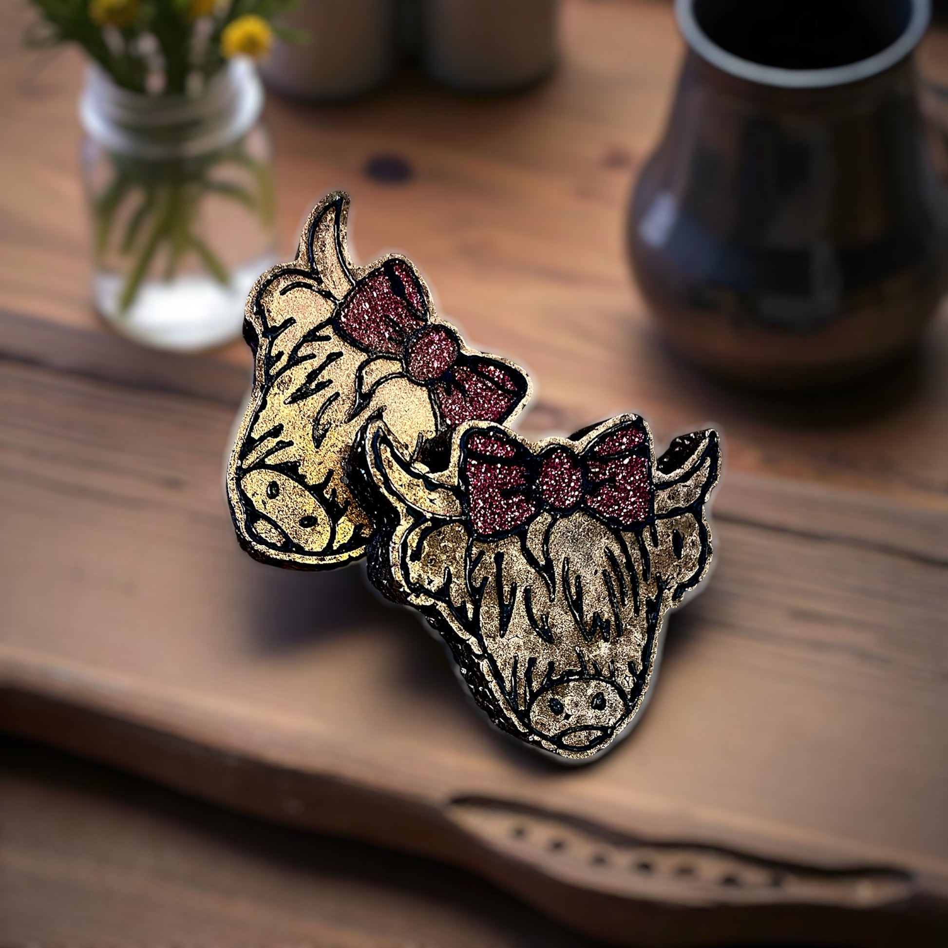 Two decorative bull skull vent clip car freshies with glittery bows on a wooden surface.