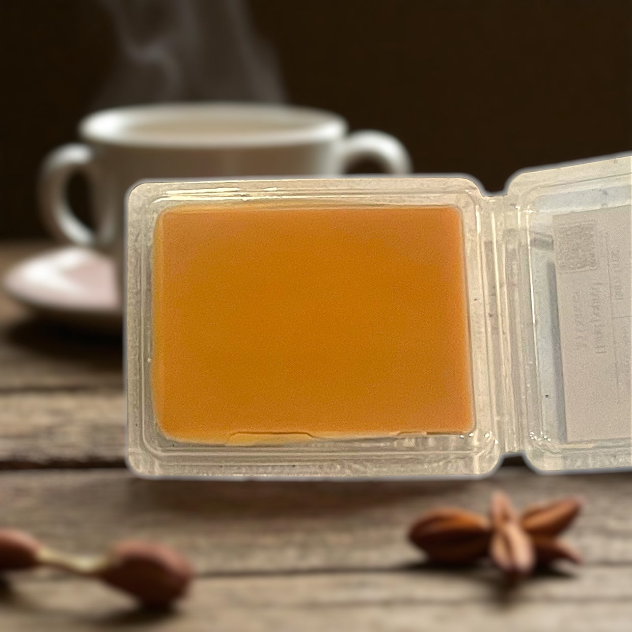 Bar wax melt bar showing the smooth color and blend of soy and beeswax in a clear container on a wooden surface with a cup and cinnamon sticks in the background.