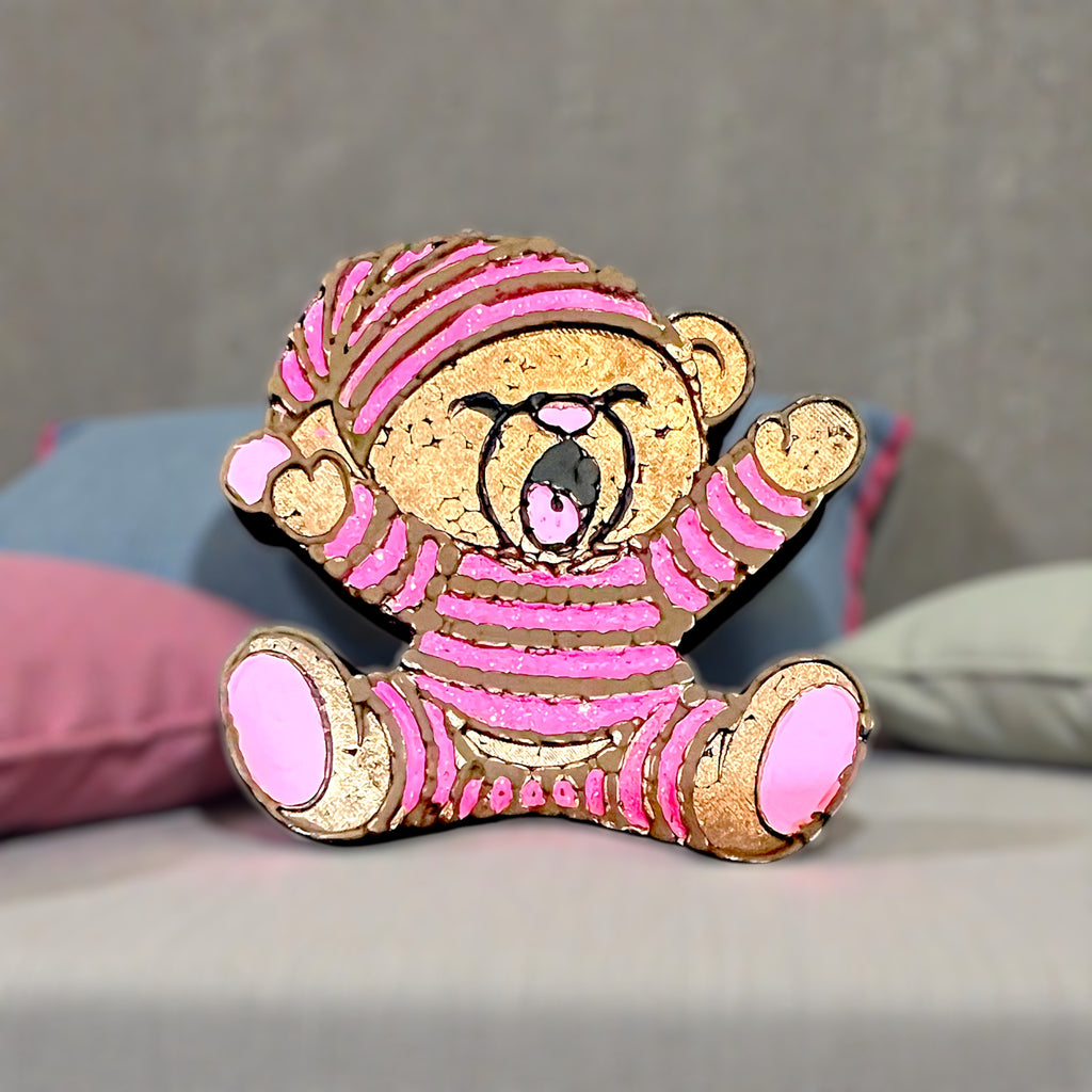 Brown Bear car freshie in pink glitter pajamas. Yawning and sitting on a grey bed with pillows.