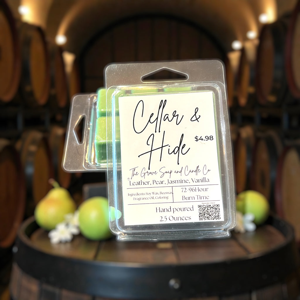 Packaged Wax Melts showing the label Cellar & Hide with the scent profile and ingredients. Sitting on a wine barrel with pears and jasmine. 
