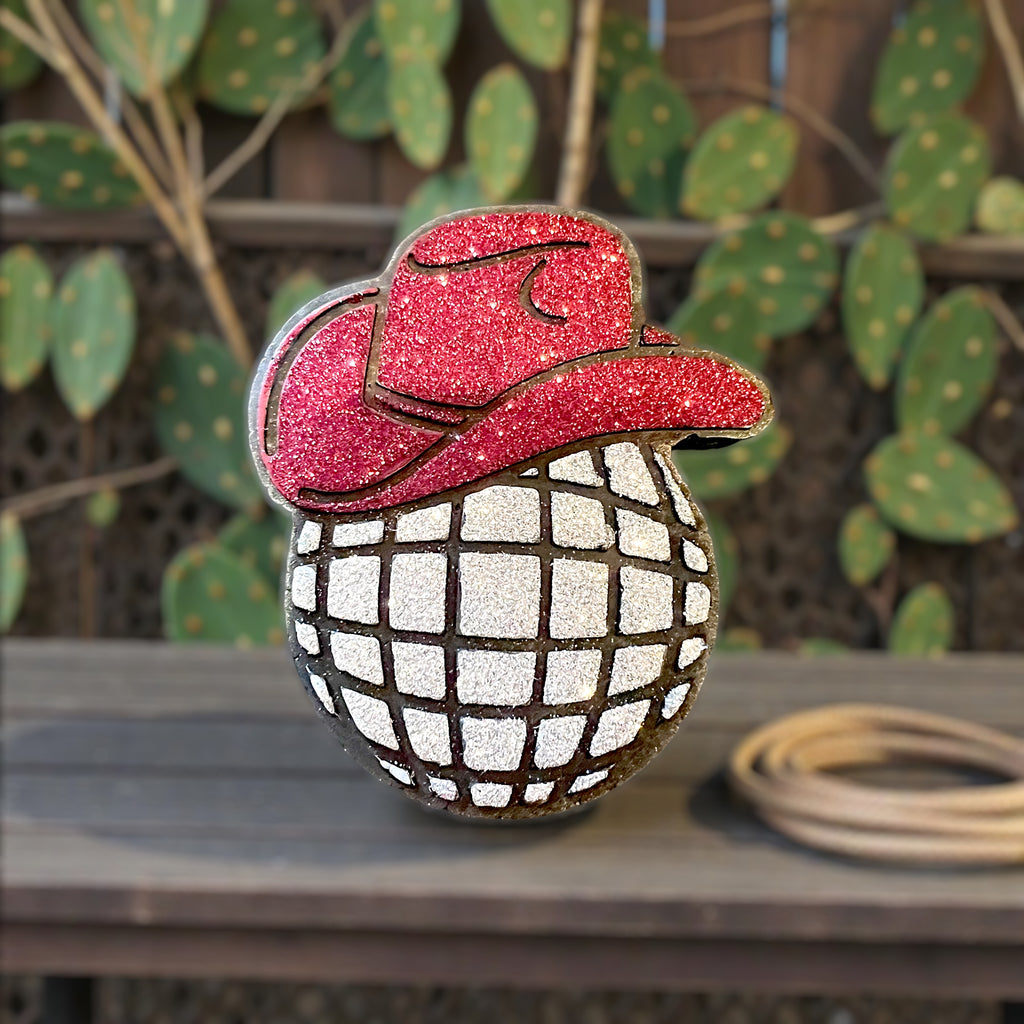 Decorative Car freshie in brown with red glitter cowboy hat and a wooden surface with a cactus plant in the background.