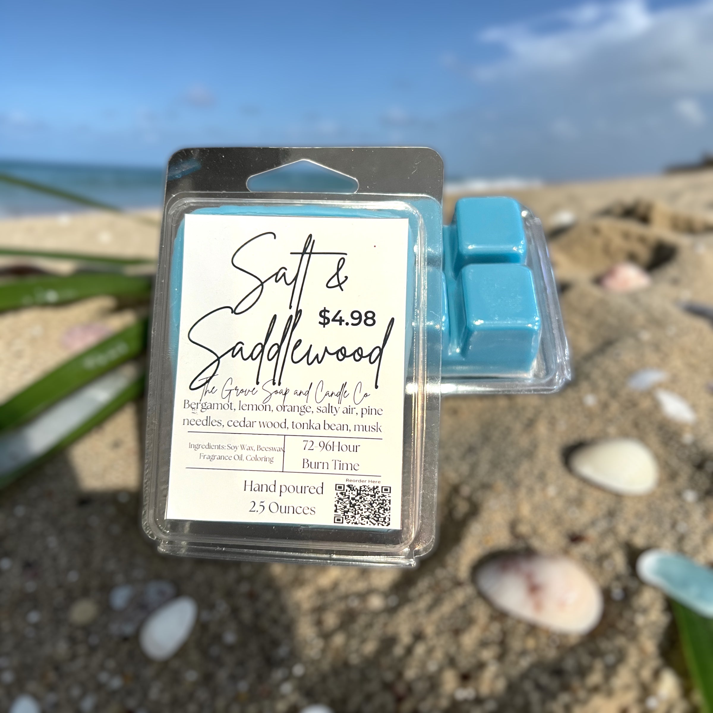 Packaged salt and saddlewood wax melts on a beach with ocean in the background. Shows the label and packaging with ingredients and scent profile. 