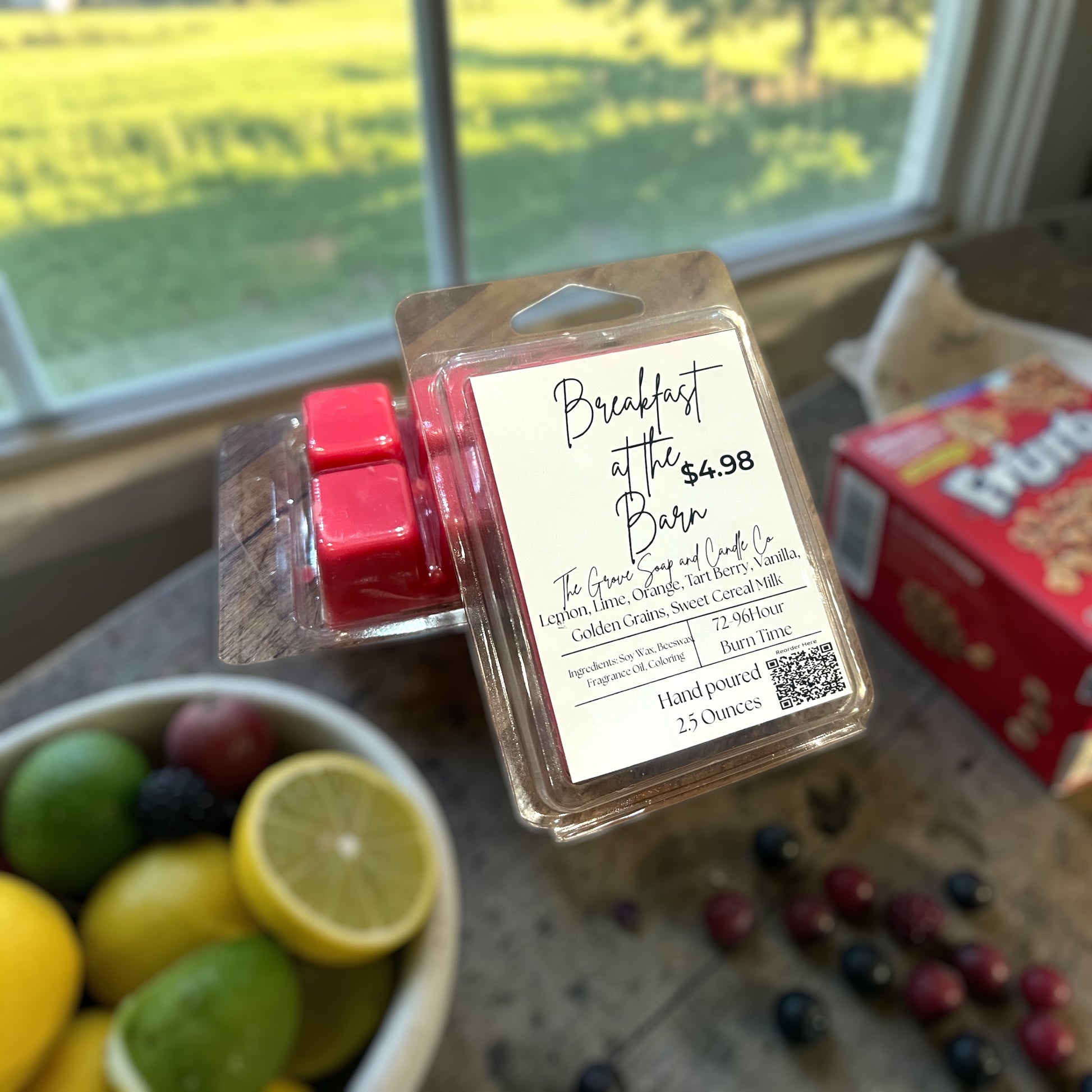 Breakfast at the Barn hand poured wax melts in a clam shell. Sitting on the table with lemons, limes, berries, and fruity cereal. Sunrise on the farm in the background.