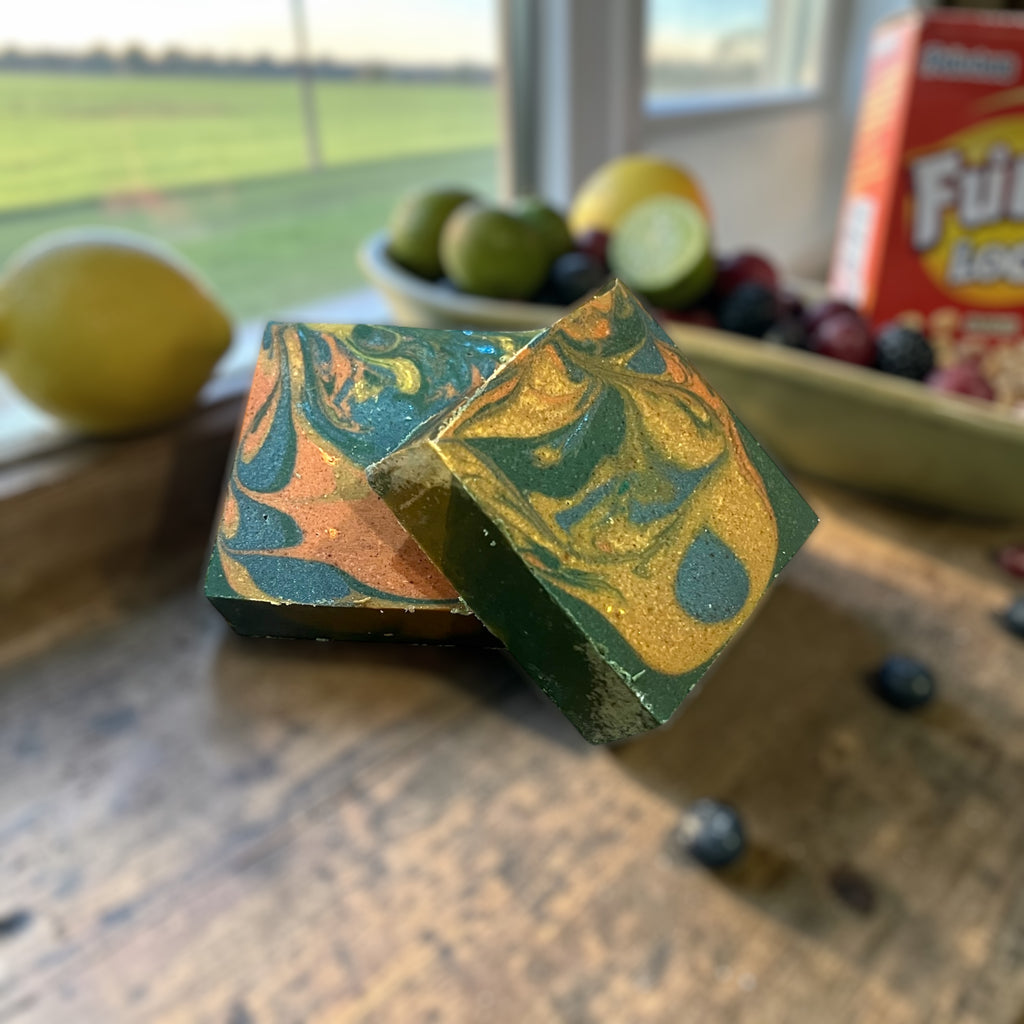 Colorful marbled Breakfast at the Barn goat Milk Soap. Sitting on a farmhouse table with lemons, limes, berries, and fruity cereal. Background is a beautiful texas sunrise.
