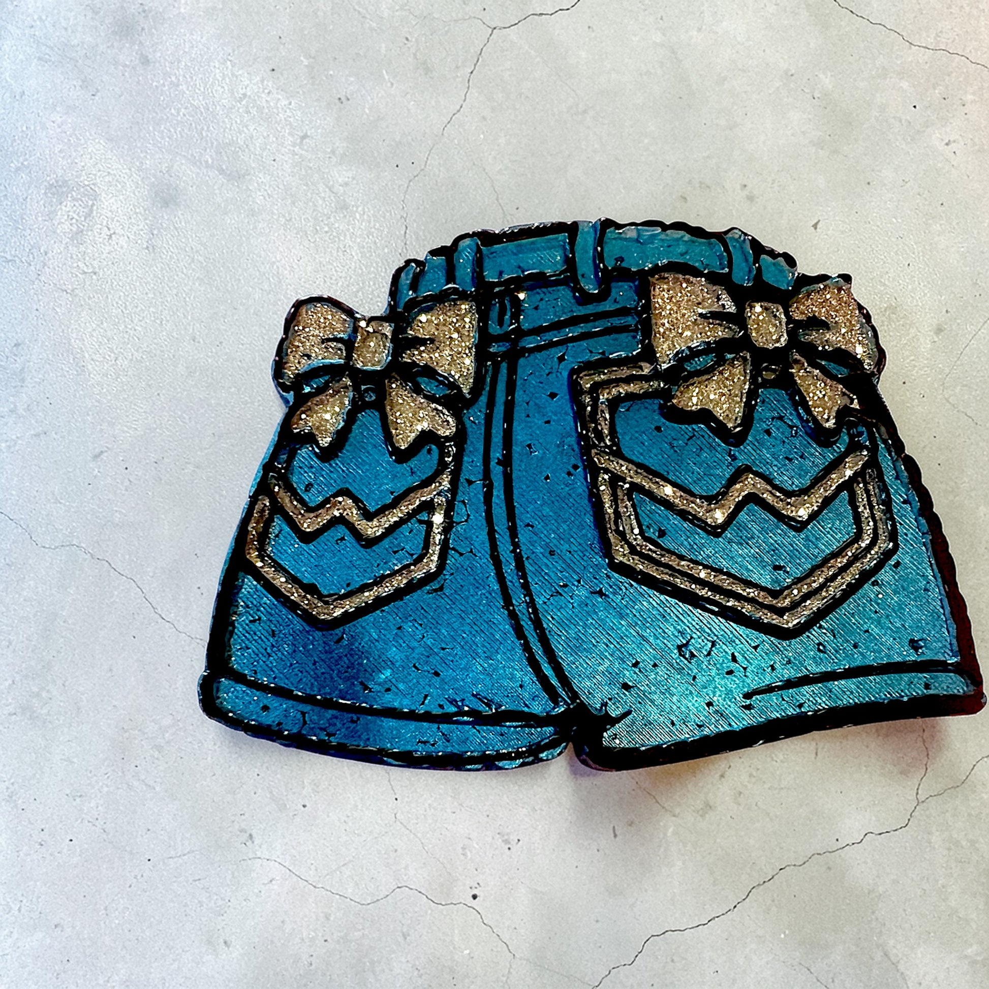 Royal blue denim shorts car freshie with silver glitter bow above the pockets and glitter accents to the pockets. Trimmed in black and on a white background. 
