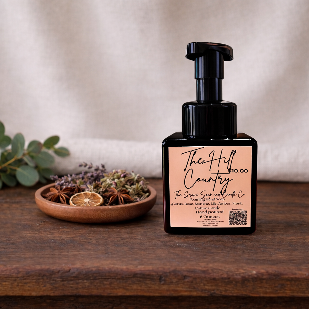 Black pump bottle with 'The Hill Country' label on a wooden surface with a bowl of dried herbs.