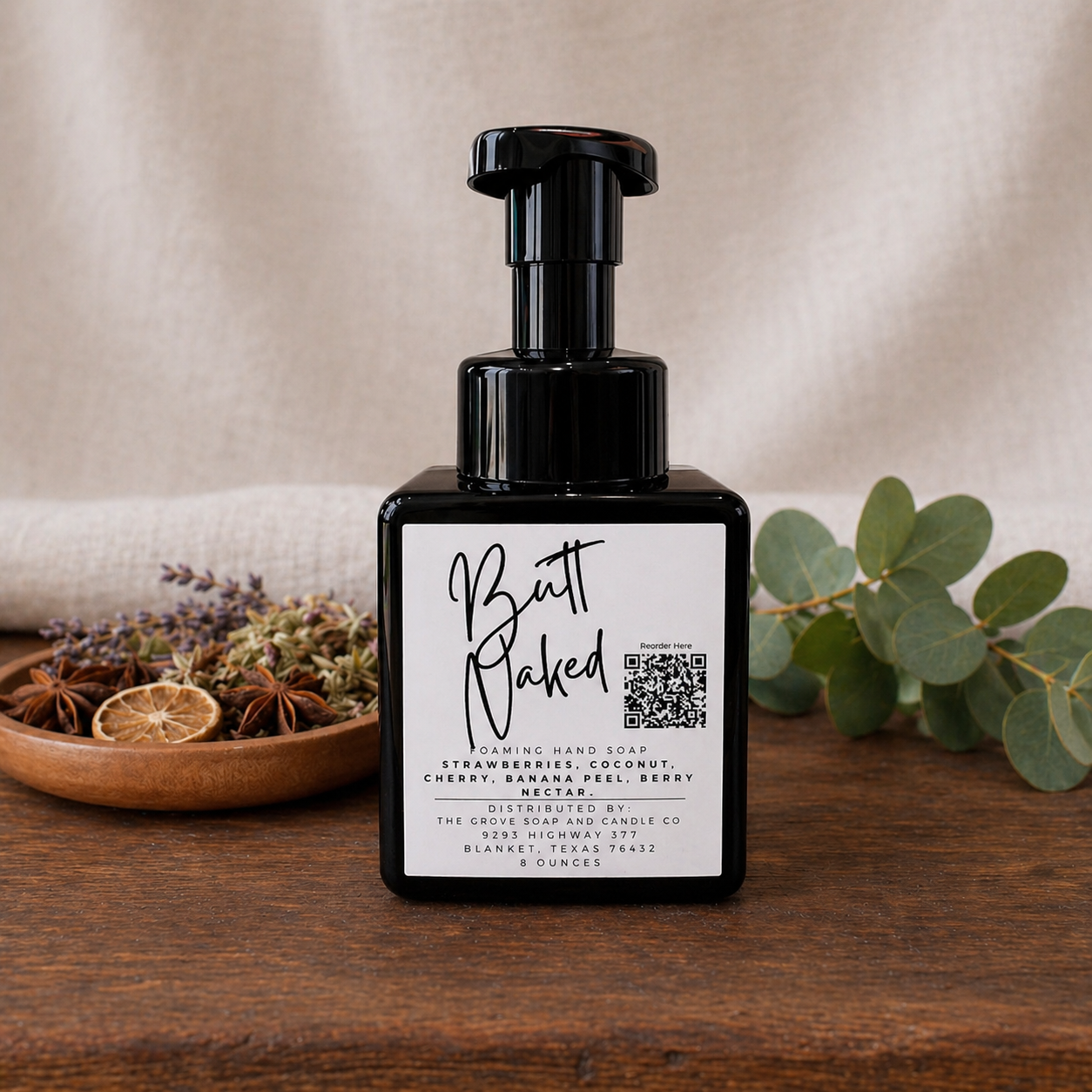 Black soap bottle with a label on a wooden surface with plants in the background