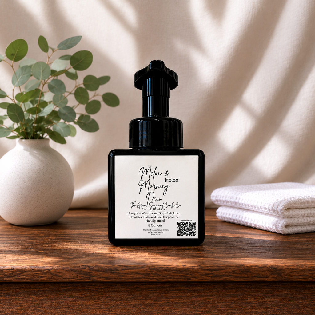 Black bottle with a white label saying Melon & Morning Dew on a wooden surface with a plant and towel in the background