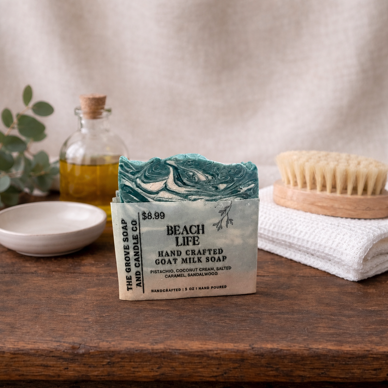 Handcrafted soap bar with packaging on a wooden surface, surrounded by a bottle, towel, and brush.