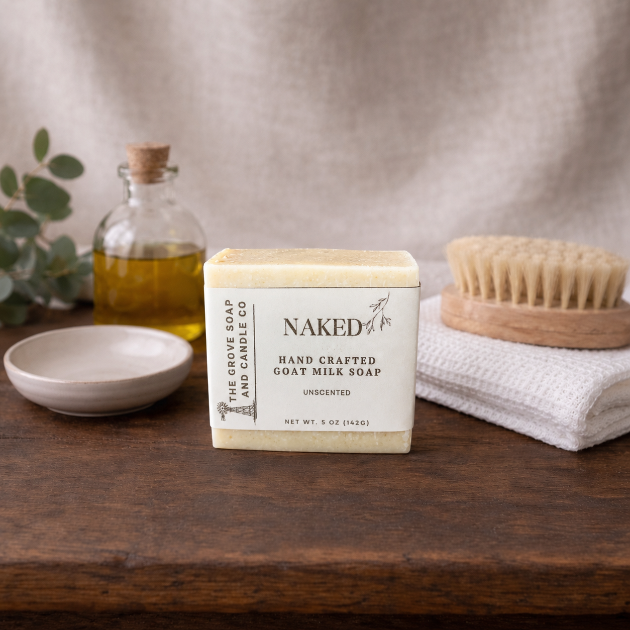 Naked Goat Milk soap bar sitting on a wooden table with bath decor in the background
