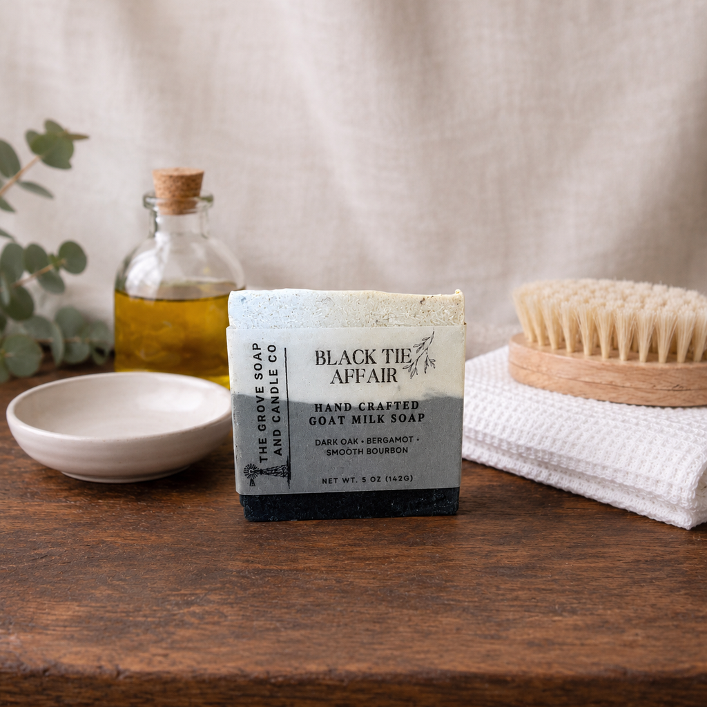 Handcrafted goat milk soap bar from 'Black The Affair' on a wooden surface with a bottle and other items.