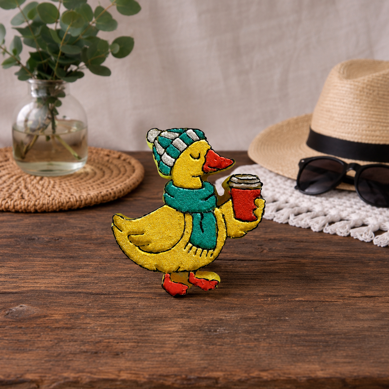 Yellow glittered duck car freshie with a light blue scarf and a blue and white beanie. holding a glittered coffee cup. 