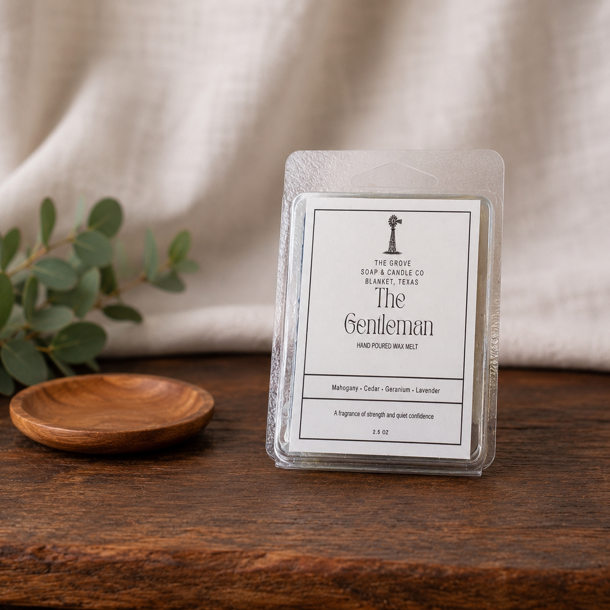 The Gentleman Wax melt sitting on a wooden table with a linen background. Shows the product labeling and sent profile
