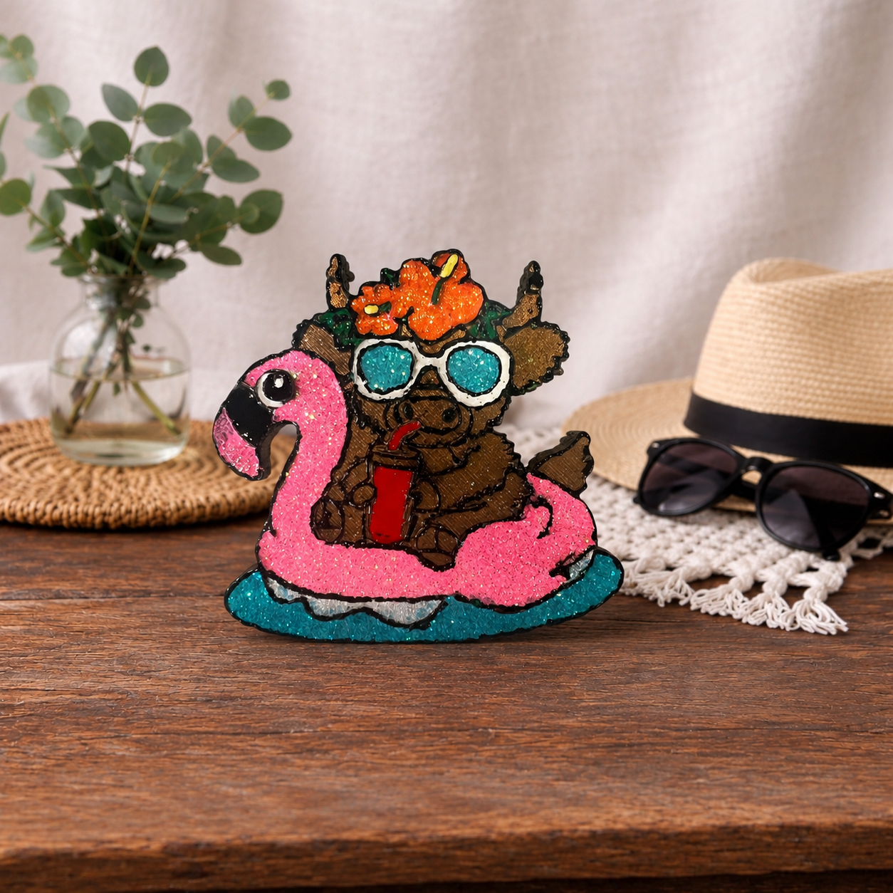 Lake Party car freshie. A highland Cow sitting on a pink glitter flamingo raft with glittered sunglasses and drinking a cold drink