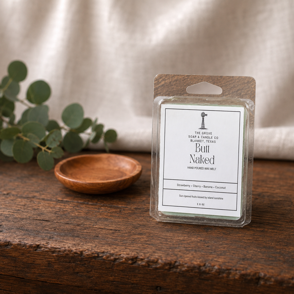A packaged wax melt product labeled 'Bull Naked' by The Grove Soap and Candle Co sits on a rustic wooden surface with a small wooden dish and eucalyptus leaves in the background against a soft neutral fabric backdrop.