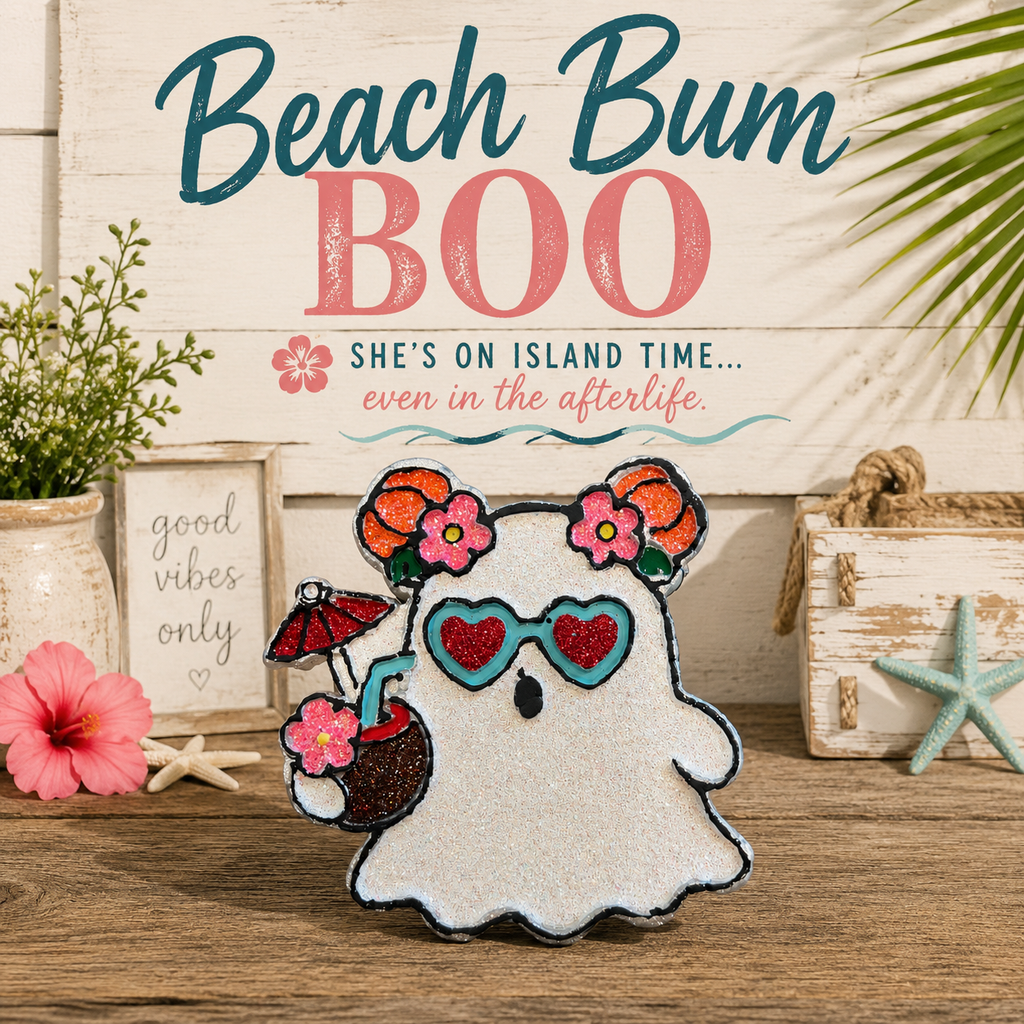 A decorative ghost-shaped car freshie with a white body, pink and orange flowers in the hair, blue heart-shaped sunglasses, and a small red umbrella accessory, displayed on a wooden surface with beach-themed props and the text 'Beach Bum BOO' in the background.