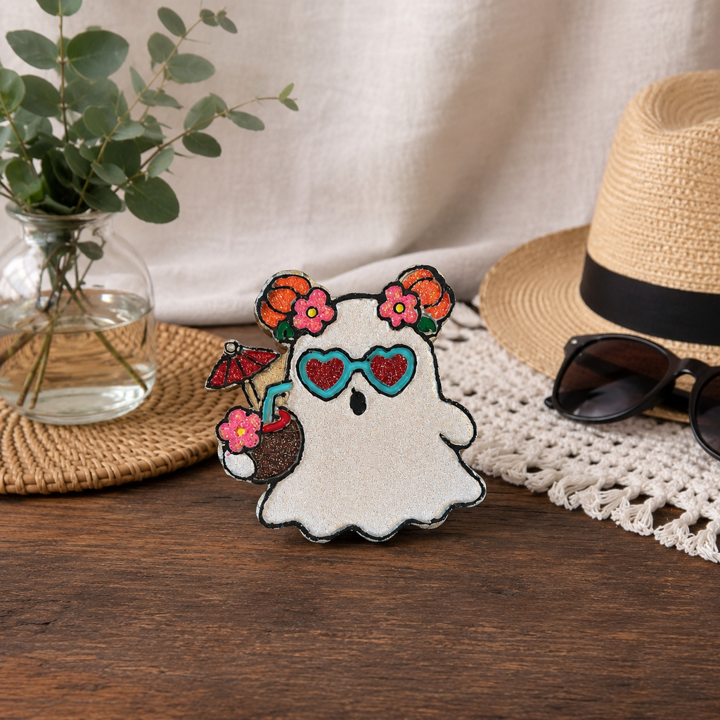 A cute ghost-shaped car freshie with pink flowers, blue heart-shaped sunglasses, and a coconut drink, styled on a wooden table with a straw hat, sunglasses, and a plant in the background.
