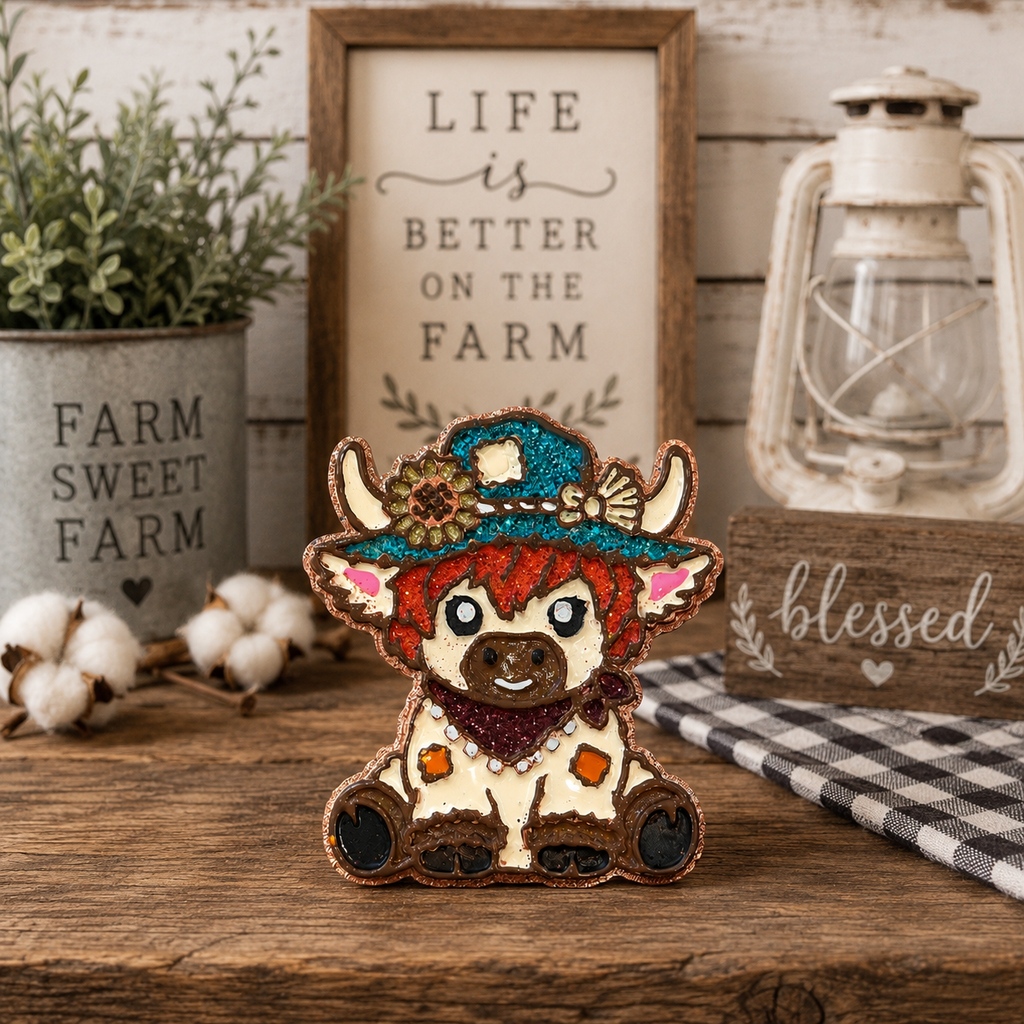 A decorative cow car freshie with a cowboy hat and bandana sits on a rustic wooden table surrounded by farmhouse-style props including a potted plant, cotton bolls, a lantern, and framed signs.