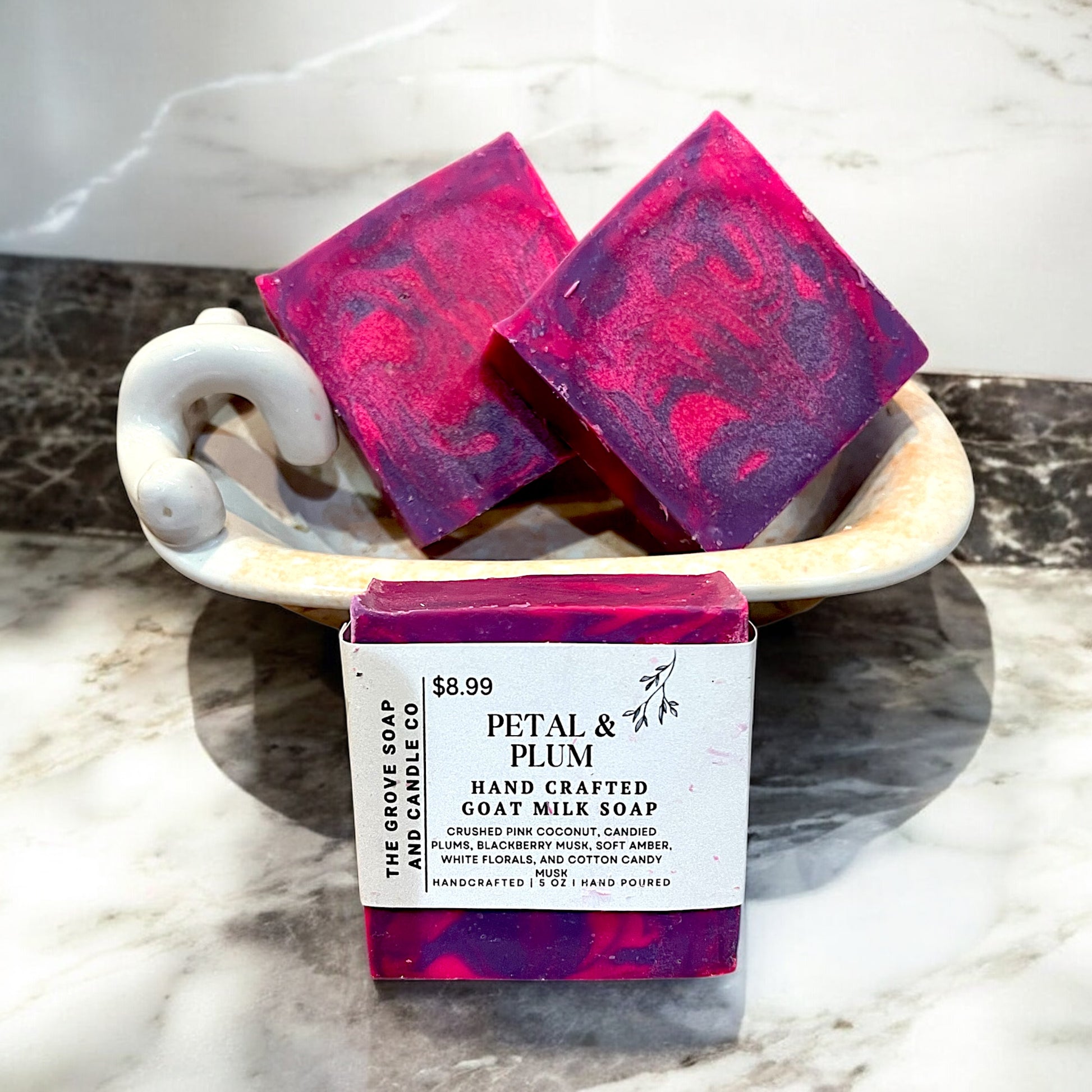 Up close photo of Petal & Plum hand crafted soap showing the label with the scent of crushed pink coconut, candied plums, white florals, blackberry musk, and cotton candy musk. 