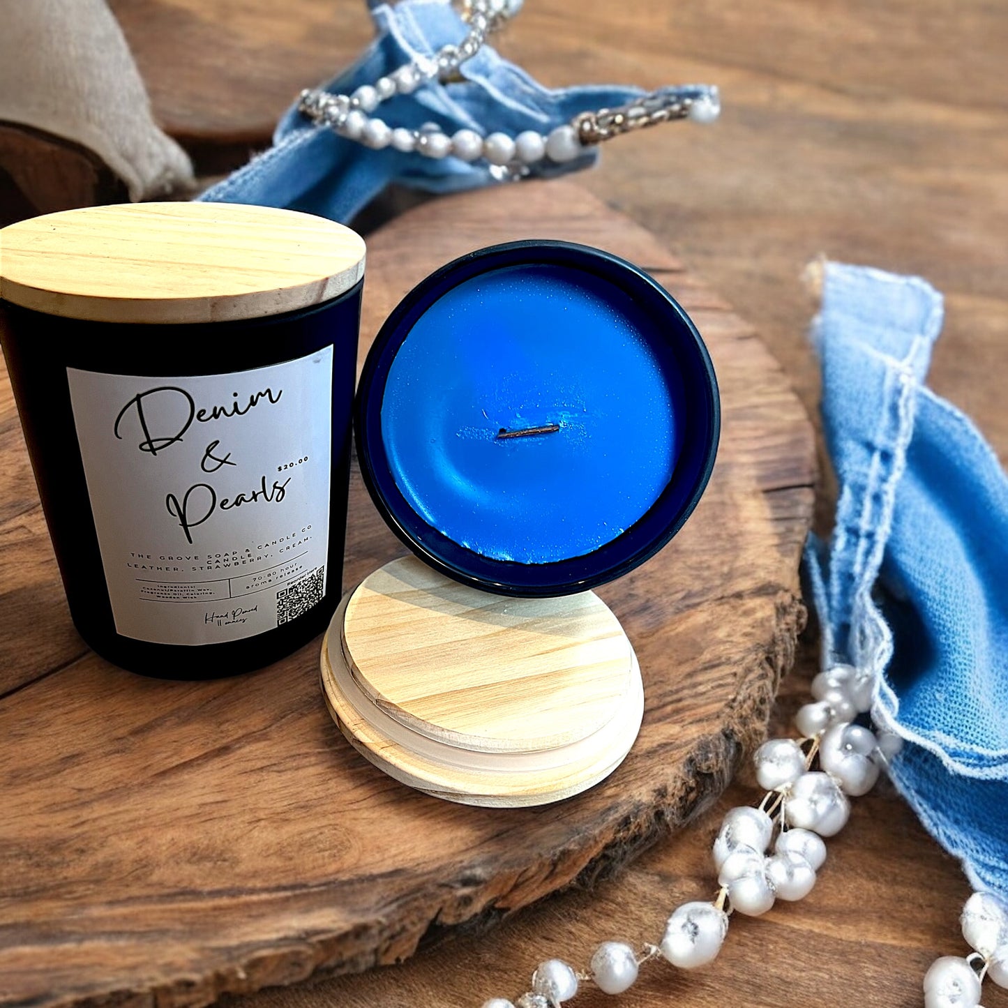Denim & Pearls candle in matte black jar with wood lid on rustic table. Showcasing the premium wax blend that is packed with the aroma of leather and strawberries and cream. 