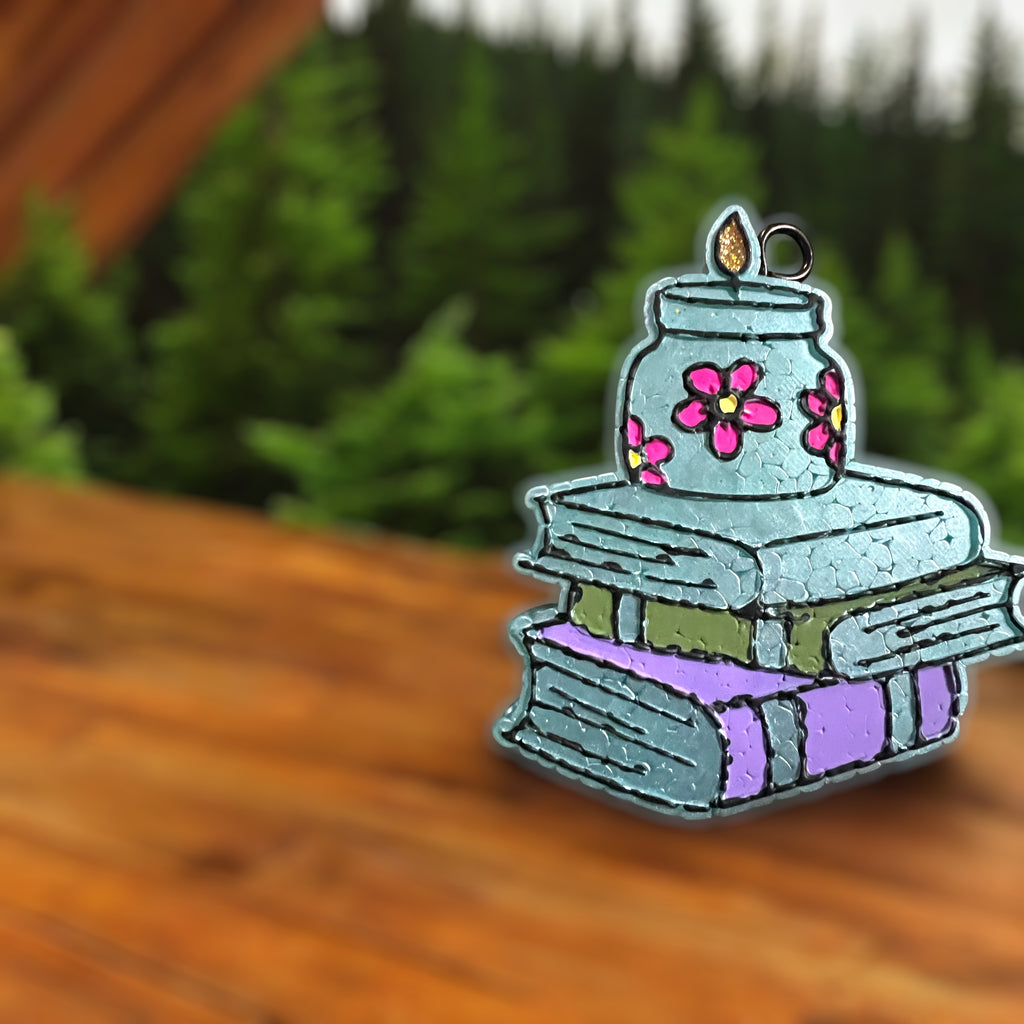 Decorative car freshie with a jar and books on a wooden surface with greenery in the background