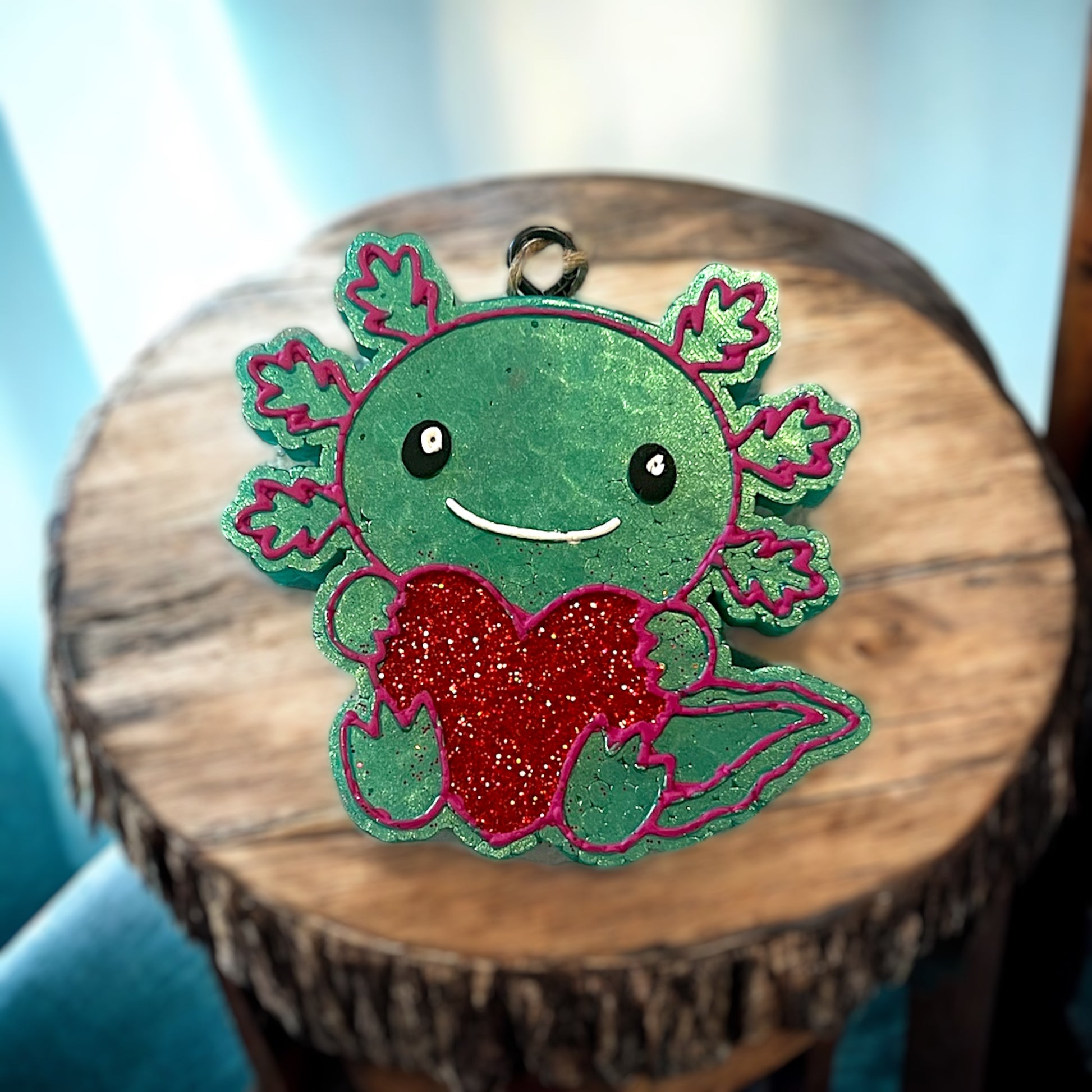 Green axolotl car freshie with a red heart on a wooden surface