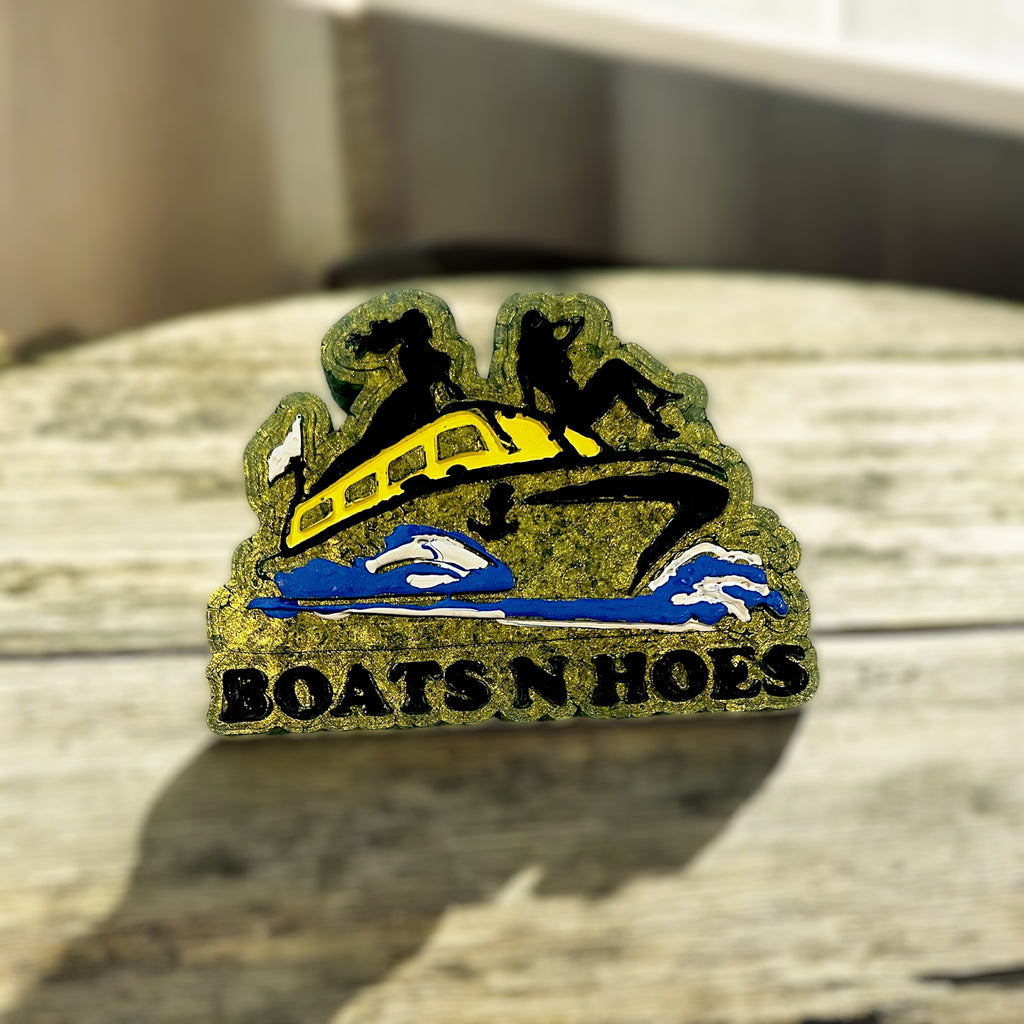 Decorative car freshie with 'BOATS N HOES' text on a textured surface
