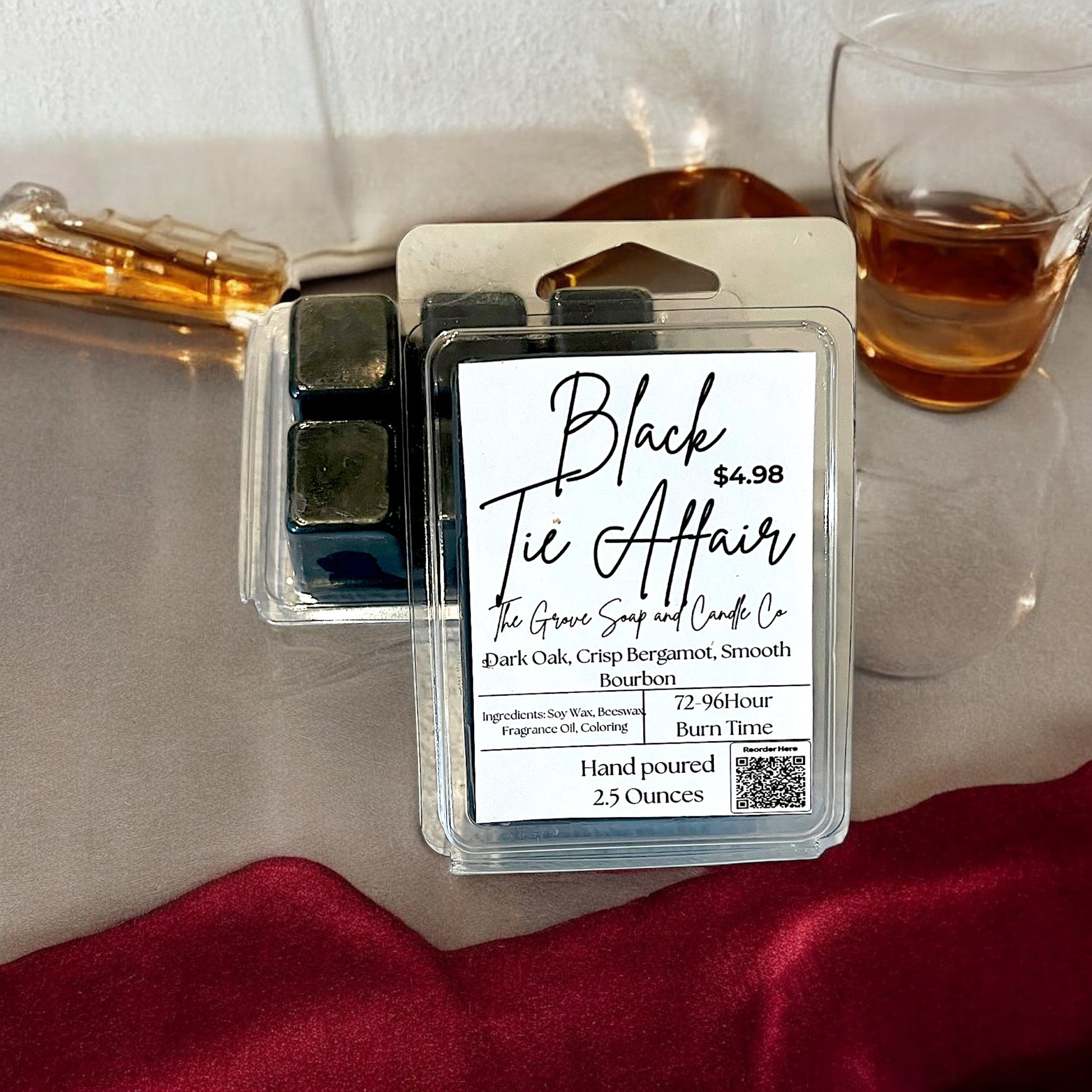 Black Tie Affair wax melts packaging with a glass of bourbon and a purse on a table. Label shows the hand poured 2.5 ounce clamshell scent in dark oak, bergamot, and bourbon. 
