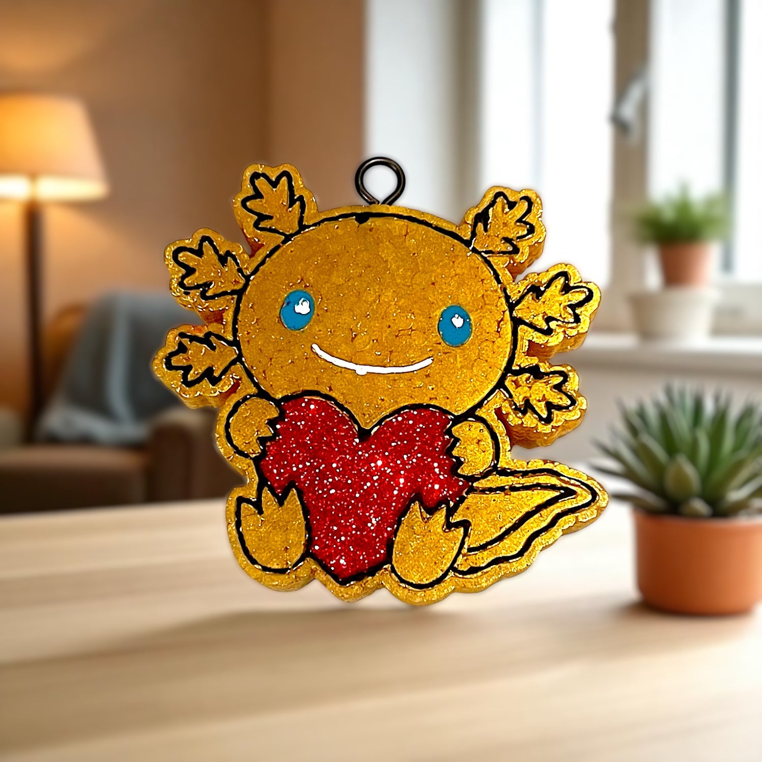 Gold axolotl with a red glittered heart on a wooden surface.