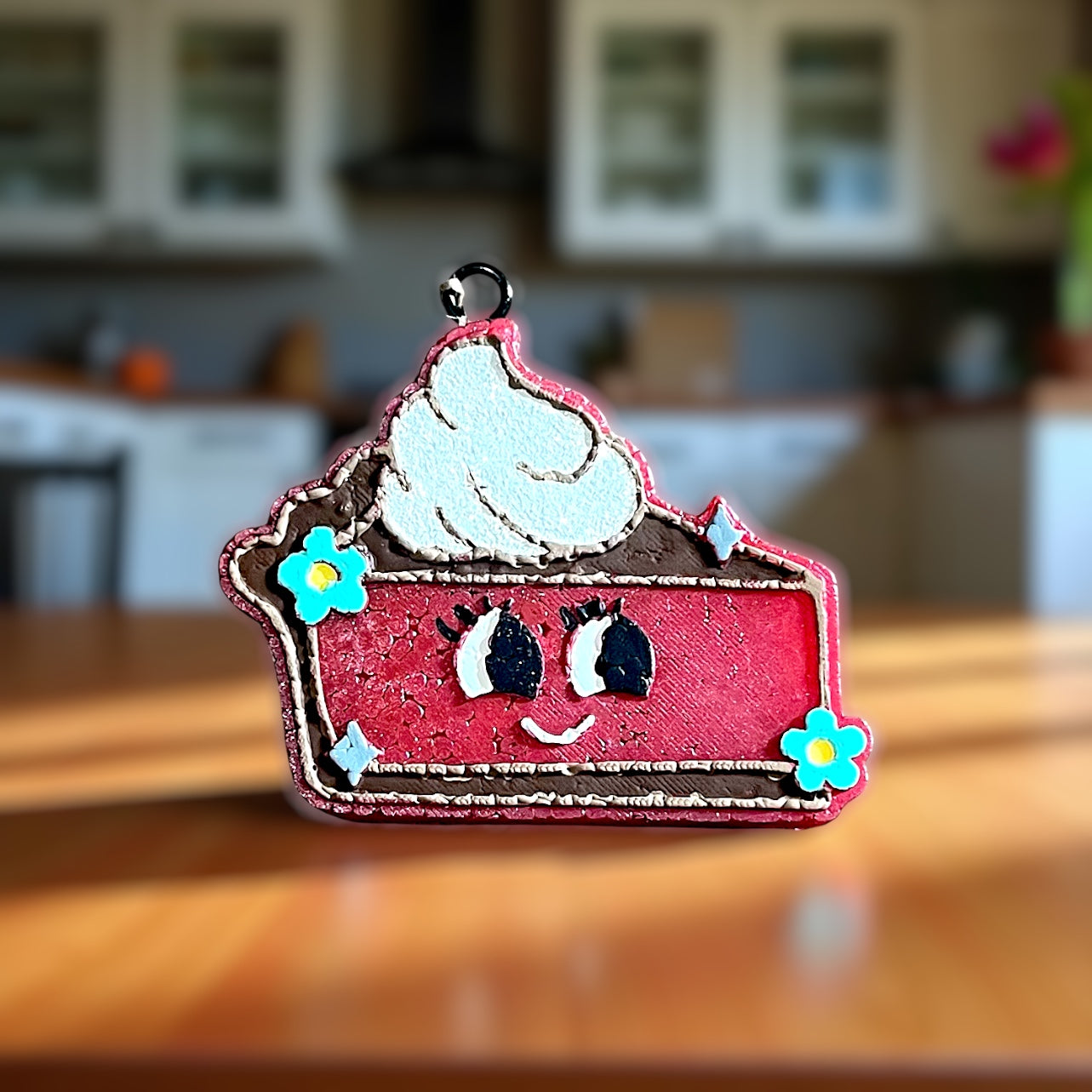 Decorative pie shape car freshie with a face on a wooden surface. Showing the bright colors to depict the aroma of cherry pie. 
