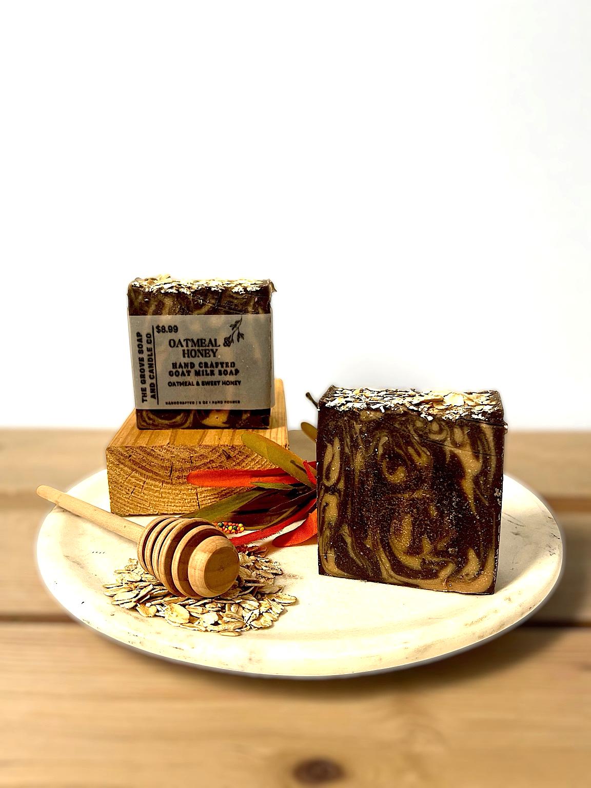 Two bars of our Oatmeal & Honey Goat Milk soap on a white plate with a honey dipper and honeycomb on a wooden surface.