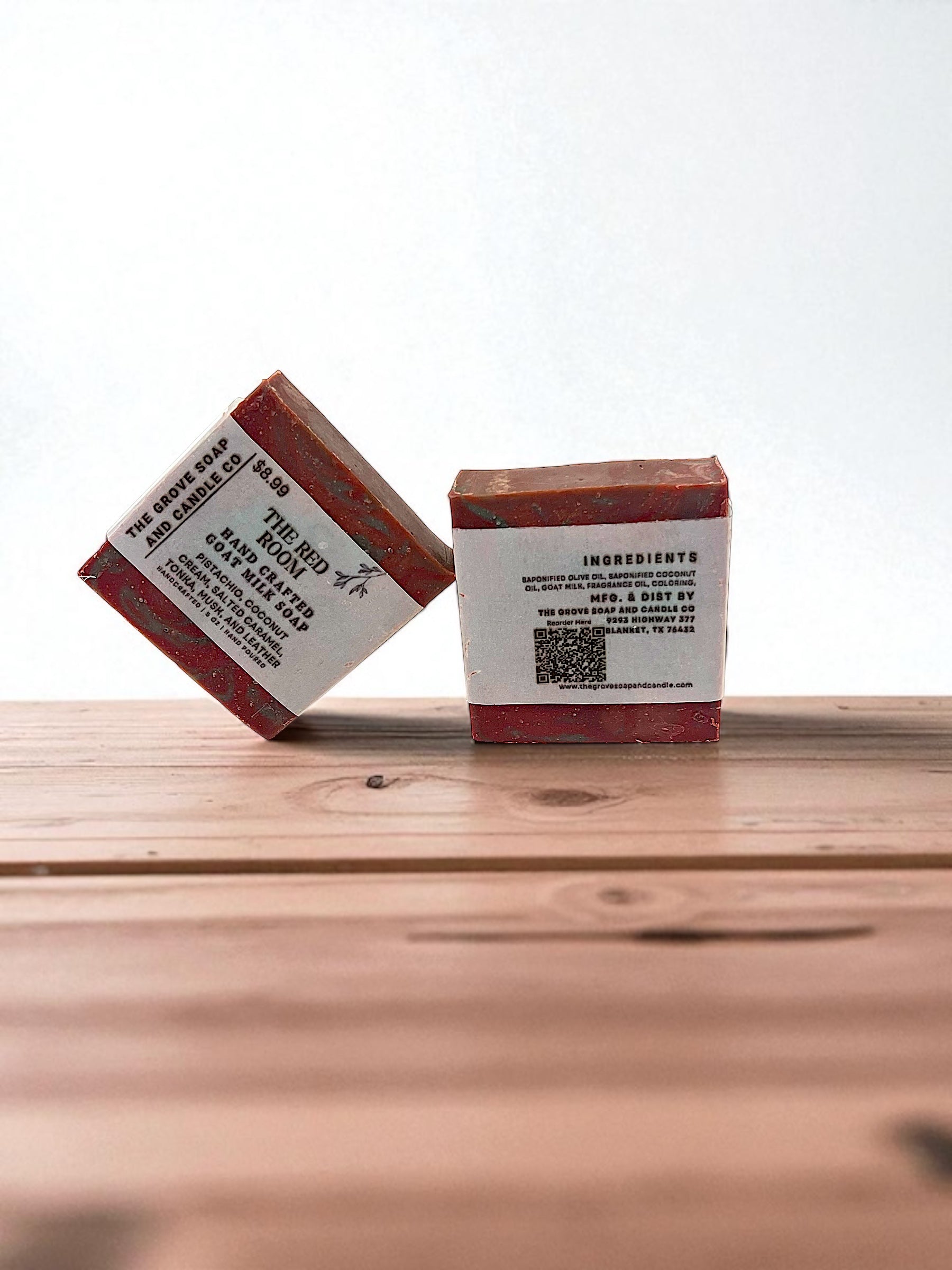 Two red and white soap bars on a wooden surface with a white background. Shows the ingredients on the label of this bar of soap 