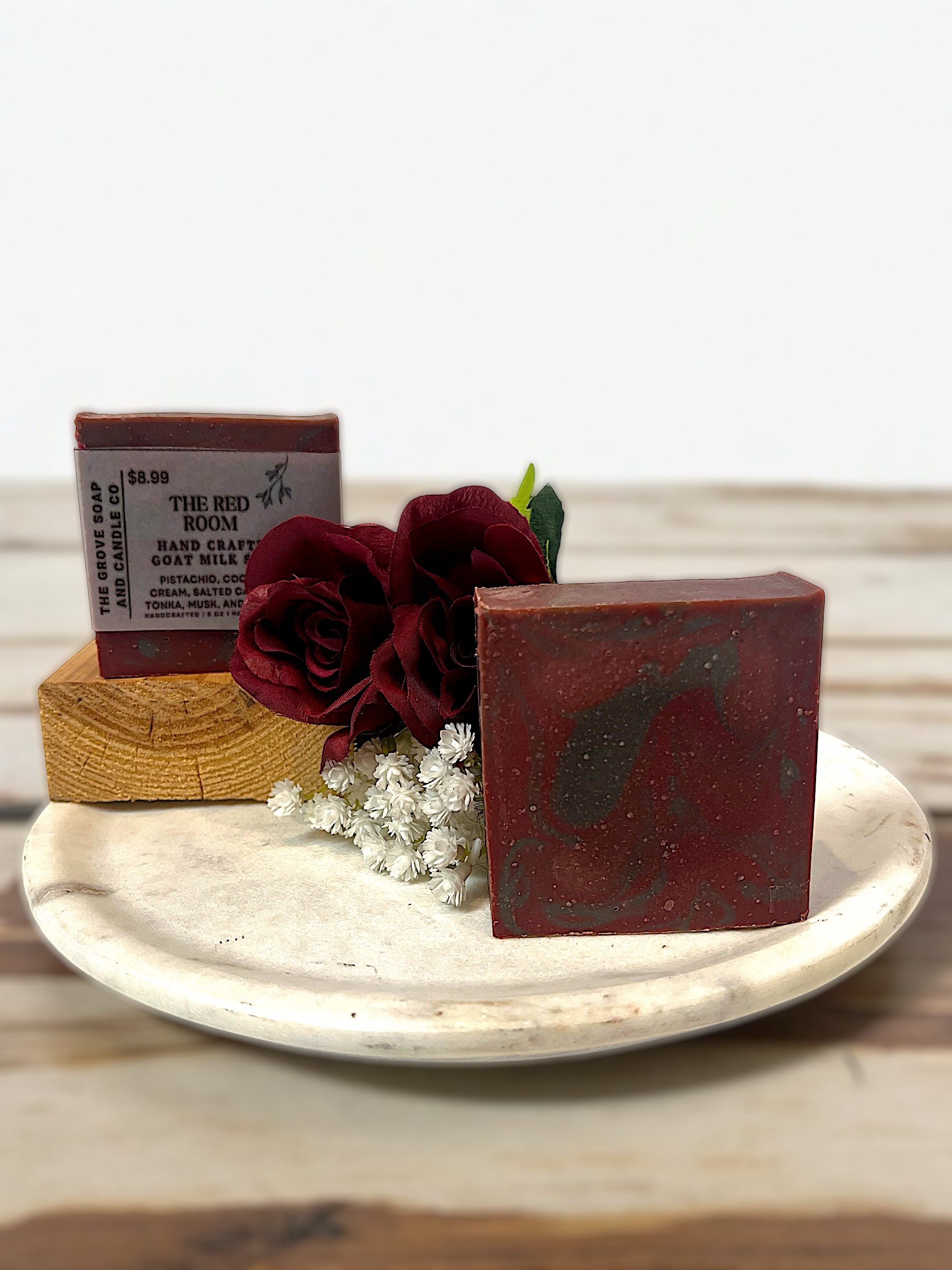 Three bars of goat milk soap on a white plate with a red rose and small white flowers, against a light background.