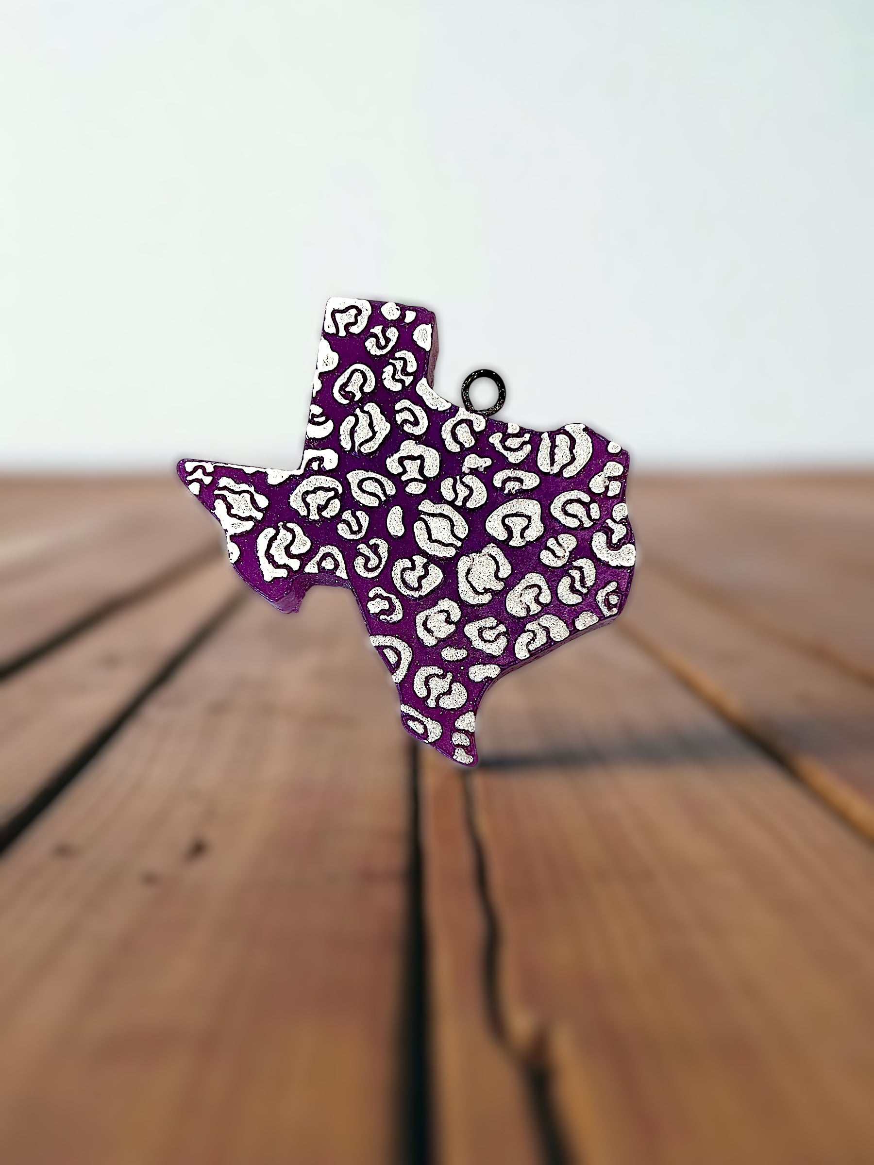 Purple and white glittered texas shaped car freshie on a wooden surface