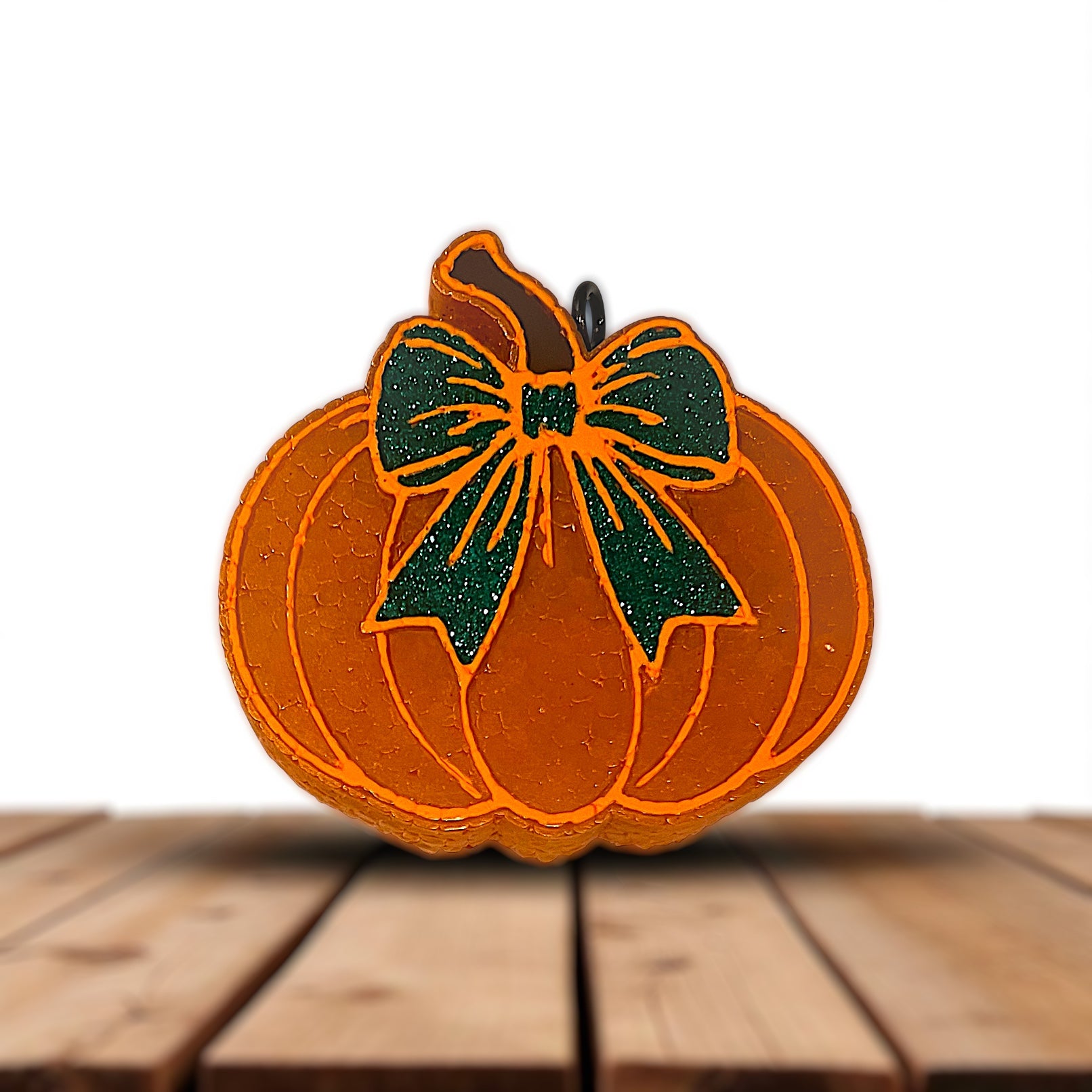Pumpkin-shaped car freshie with a green glittered bow on a wooden surface
