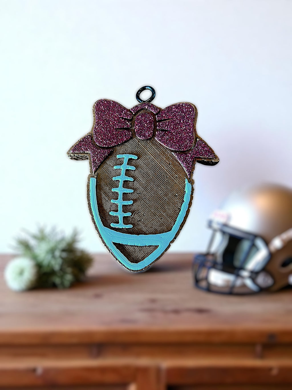 Decorative football car freshie with a maroon bow on a wooden surface.
