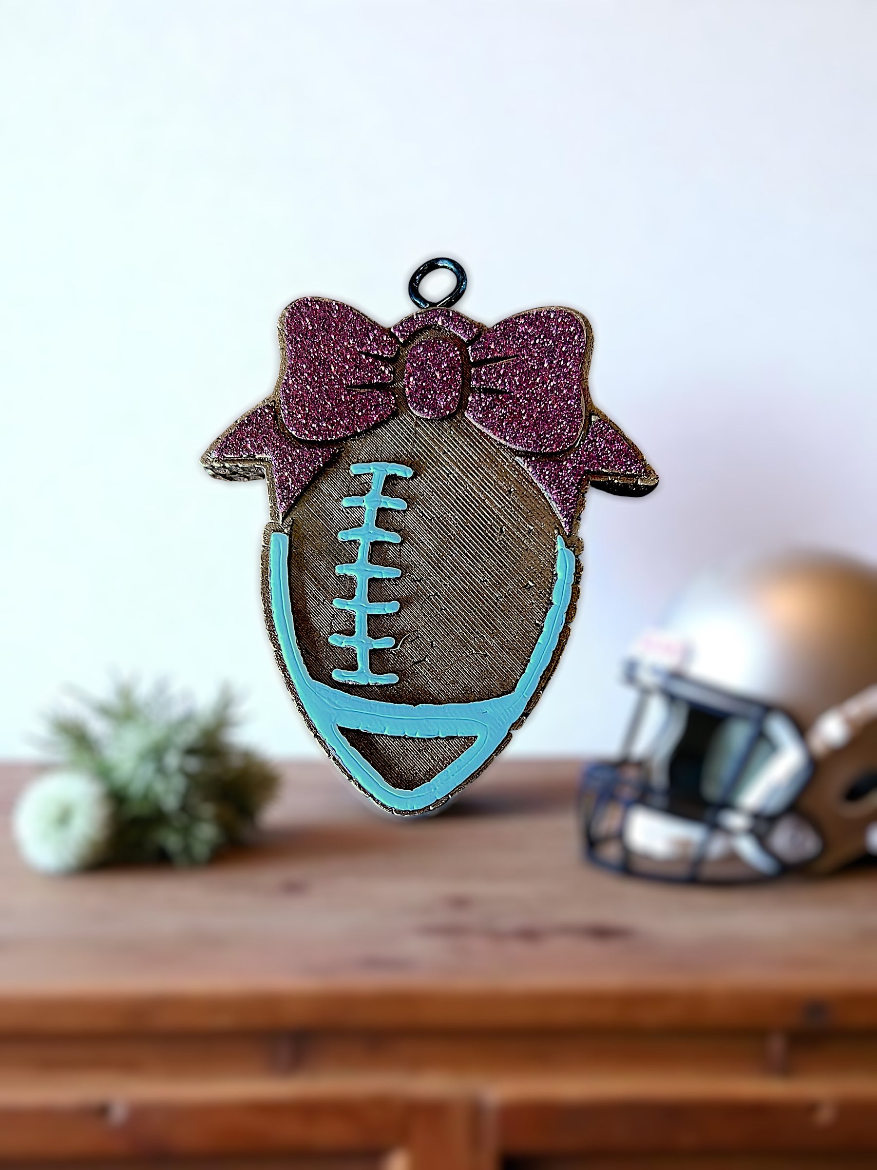 Decorative football car freshie with a maroon bow on a wooden surface.