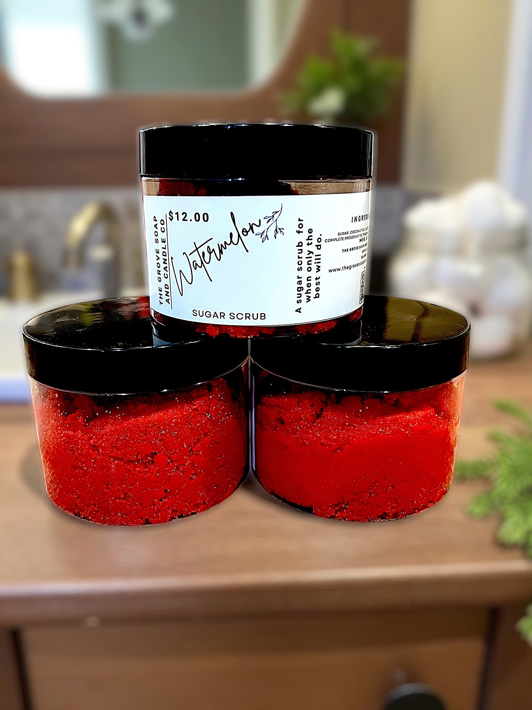 Two containers of red sugar scrub with a watermelon label on a bathroom counter.