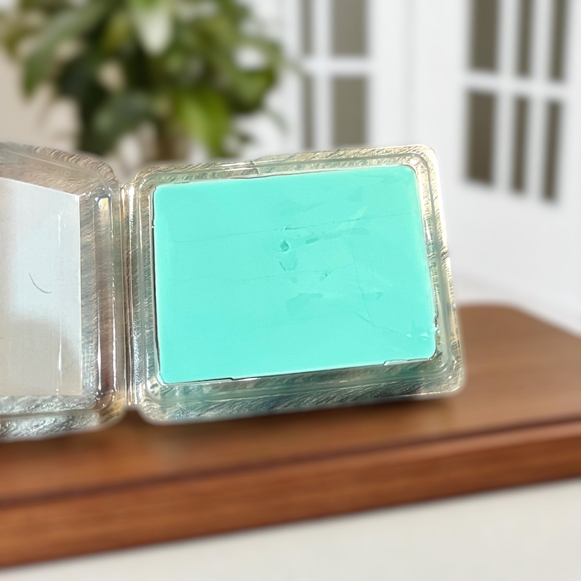 Turquoise wax melts on a wooden surface with a blurred indoor background showing the smoothness of the wax. 
