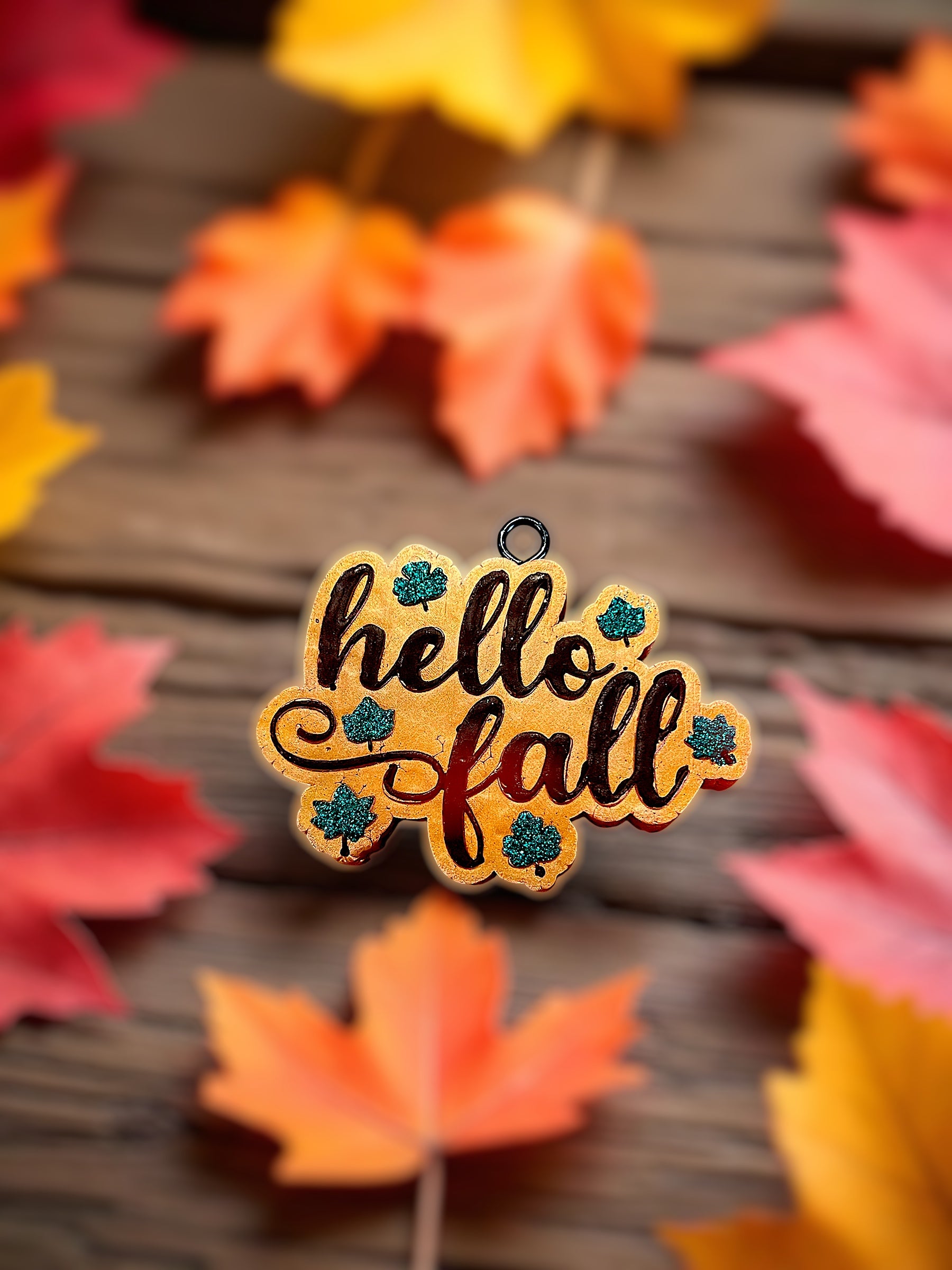 Autumn-themed 'hello fall' car freshie with colorful leaves on a wooden surface.