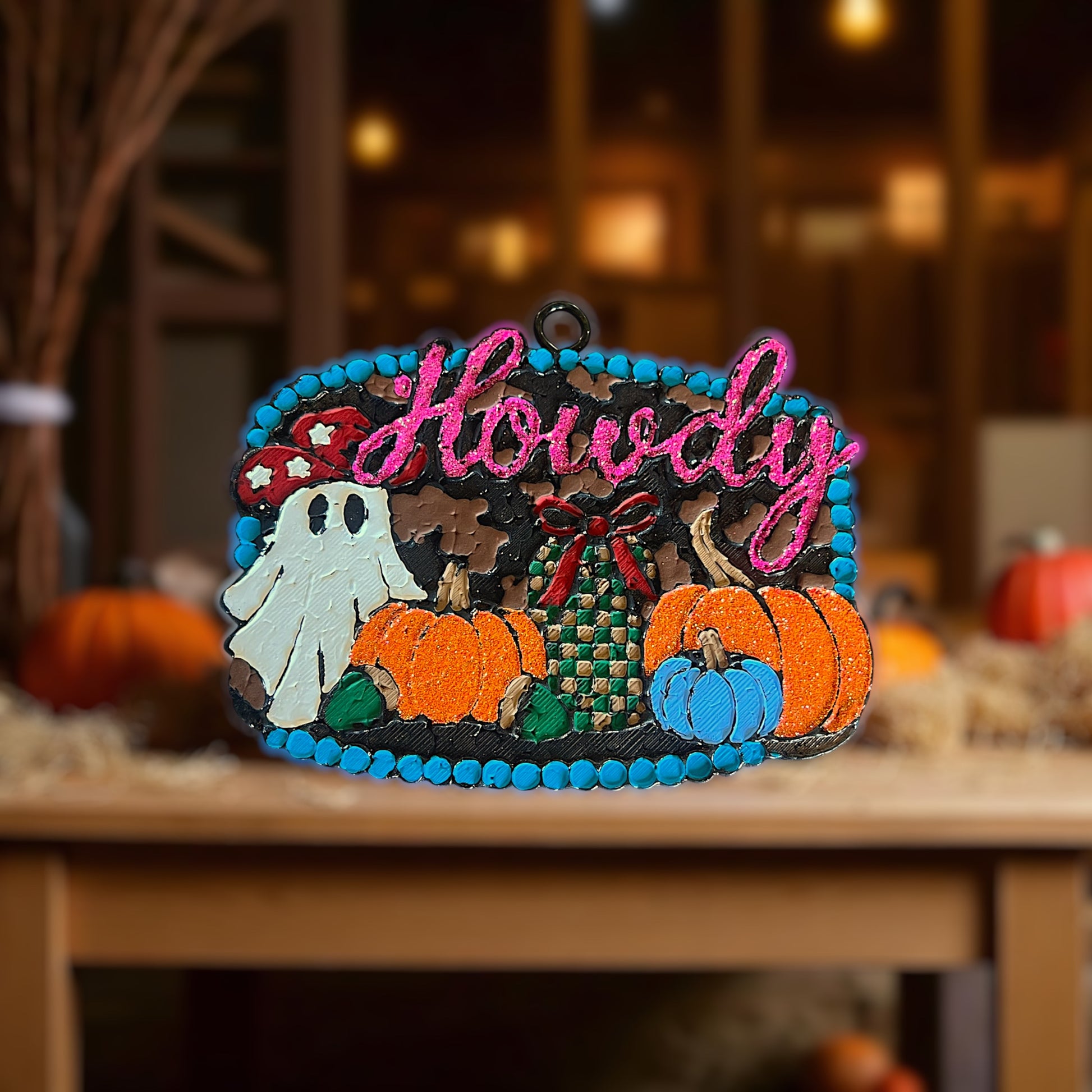 Decorative buckle car freshie with 'Howdy' text, pumpkins, and ghost on a wooden surface with blurred background.