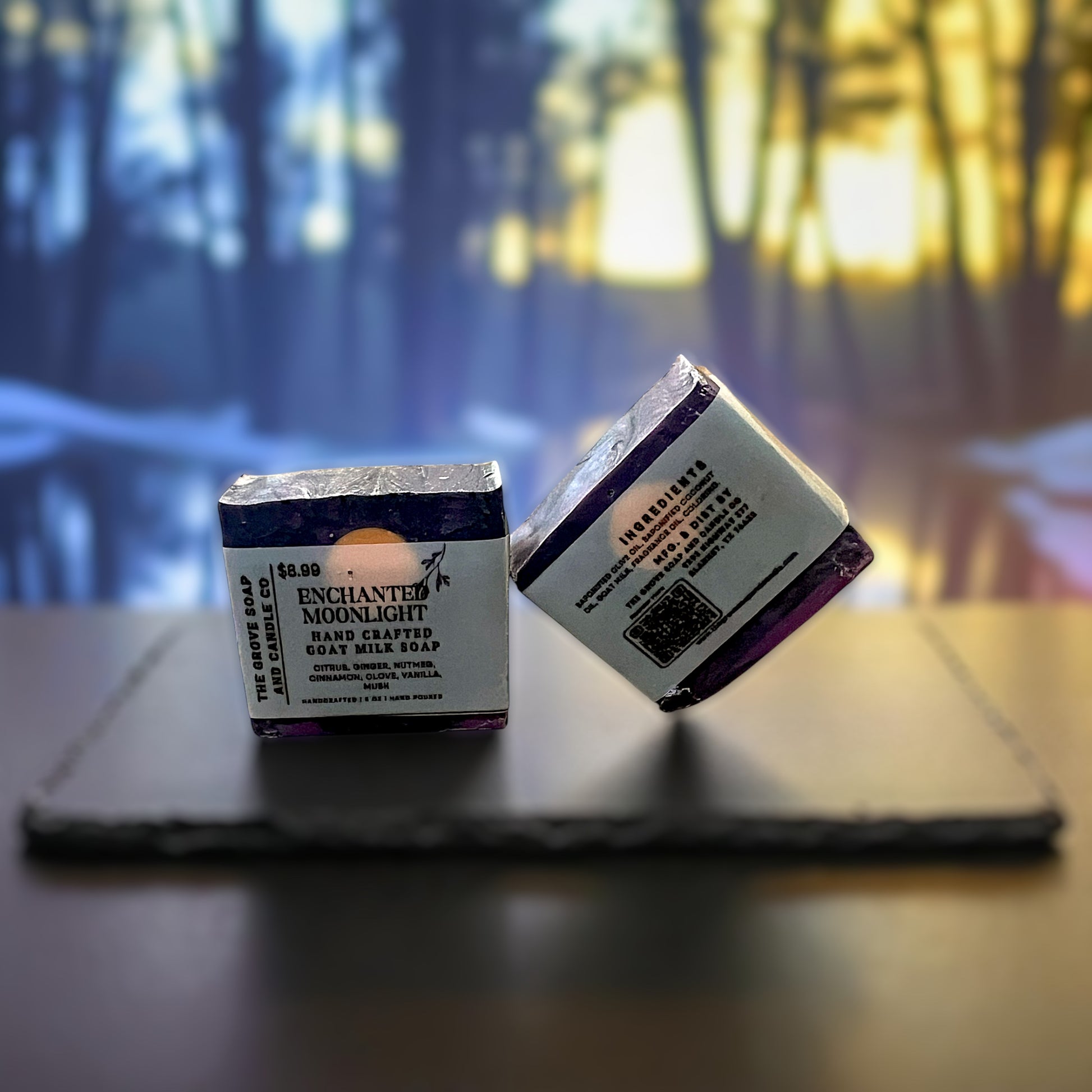 Two soap bars with packaging on a wooden surface, blurred background. Shows the name Enchanted Moonlight with a scent descritption

